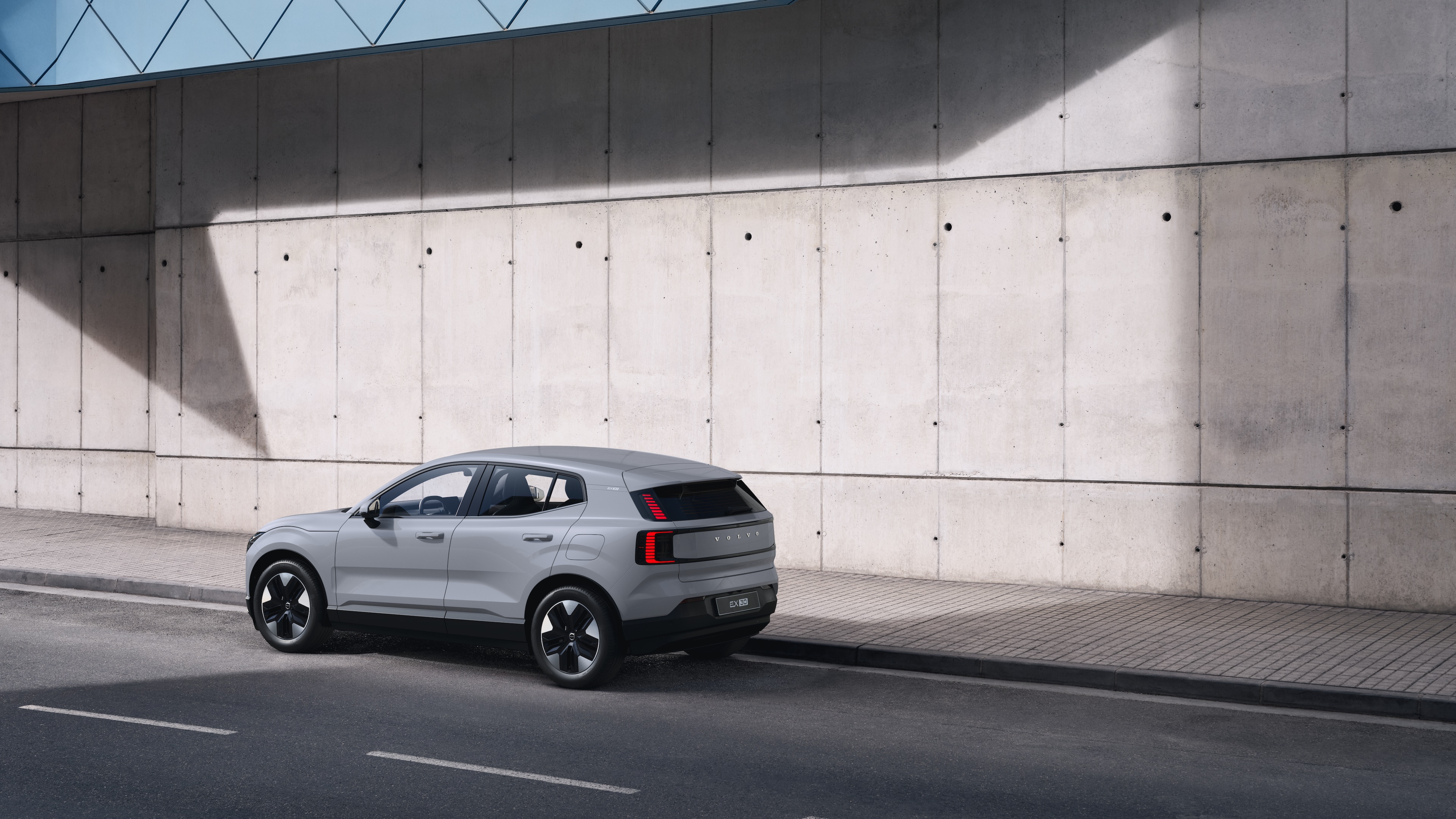 Volvo-bíll að aftan, séð þrjá fjórðu hluta úr bíl, lagt við steyptan vegg á götu í borg.
