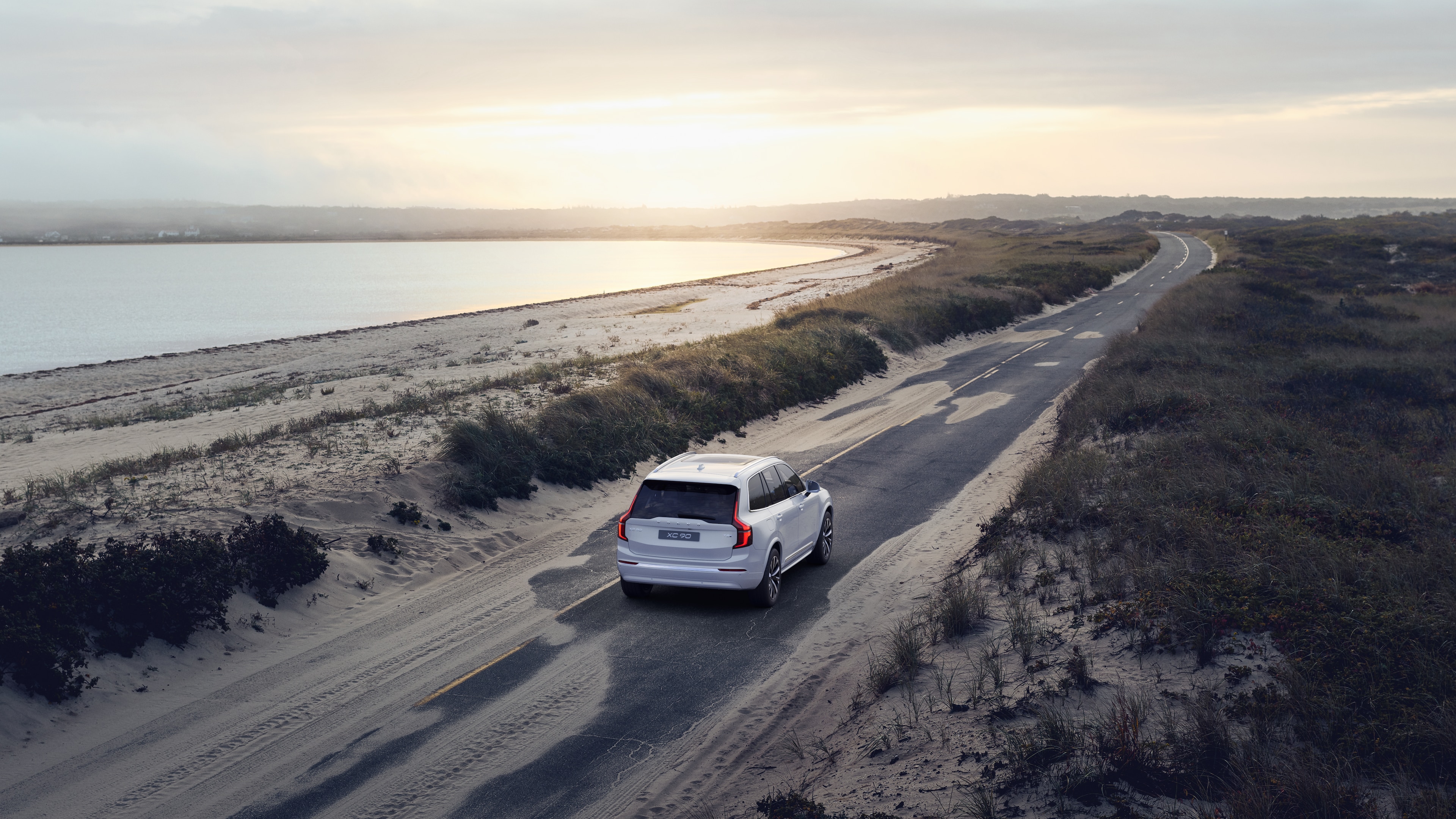 Volvo car rear view on a winding coastal road with a beachside background.