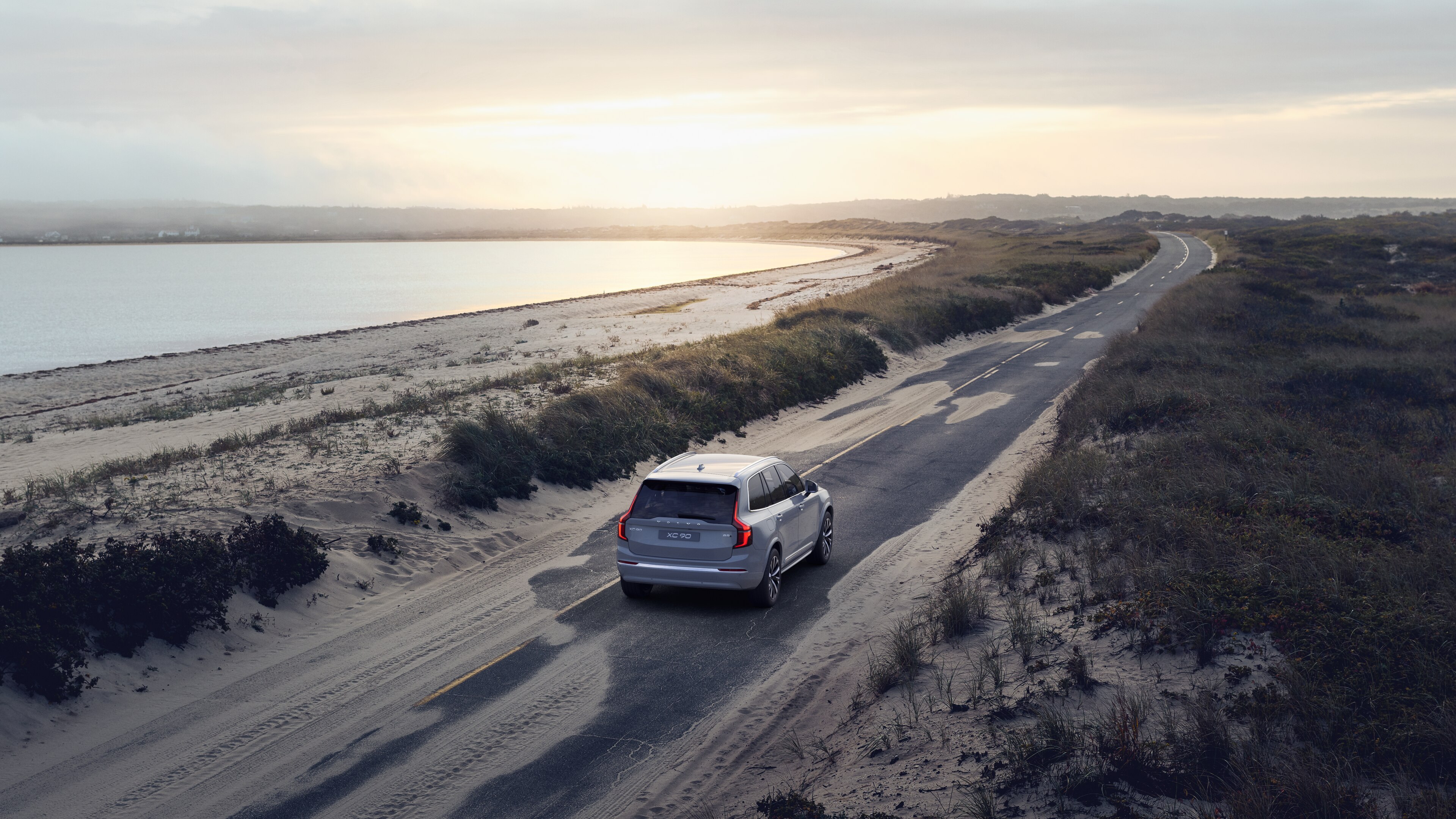 Volvo car rear view on a winding coastal road with a beachside background.