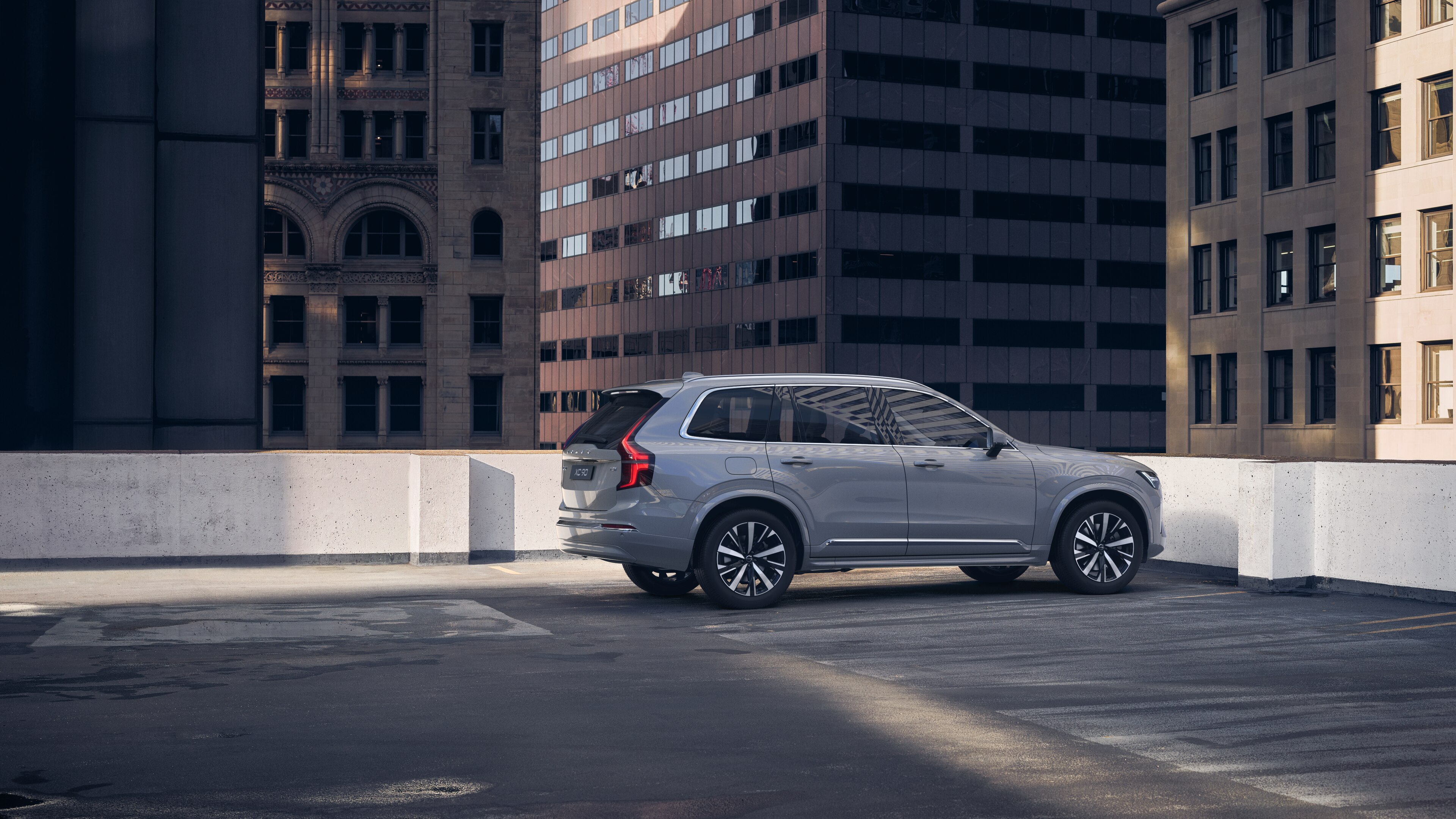 Volvo car in rear three-quarter view on an urban rooftop parking lot with surrounding tall buildings.