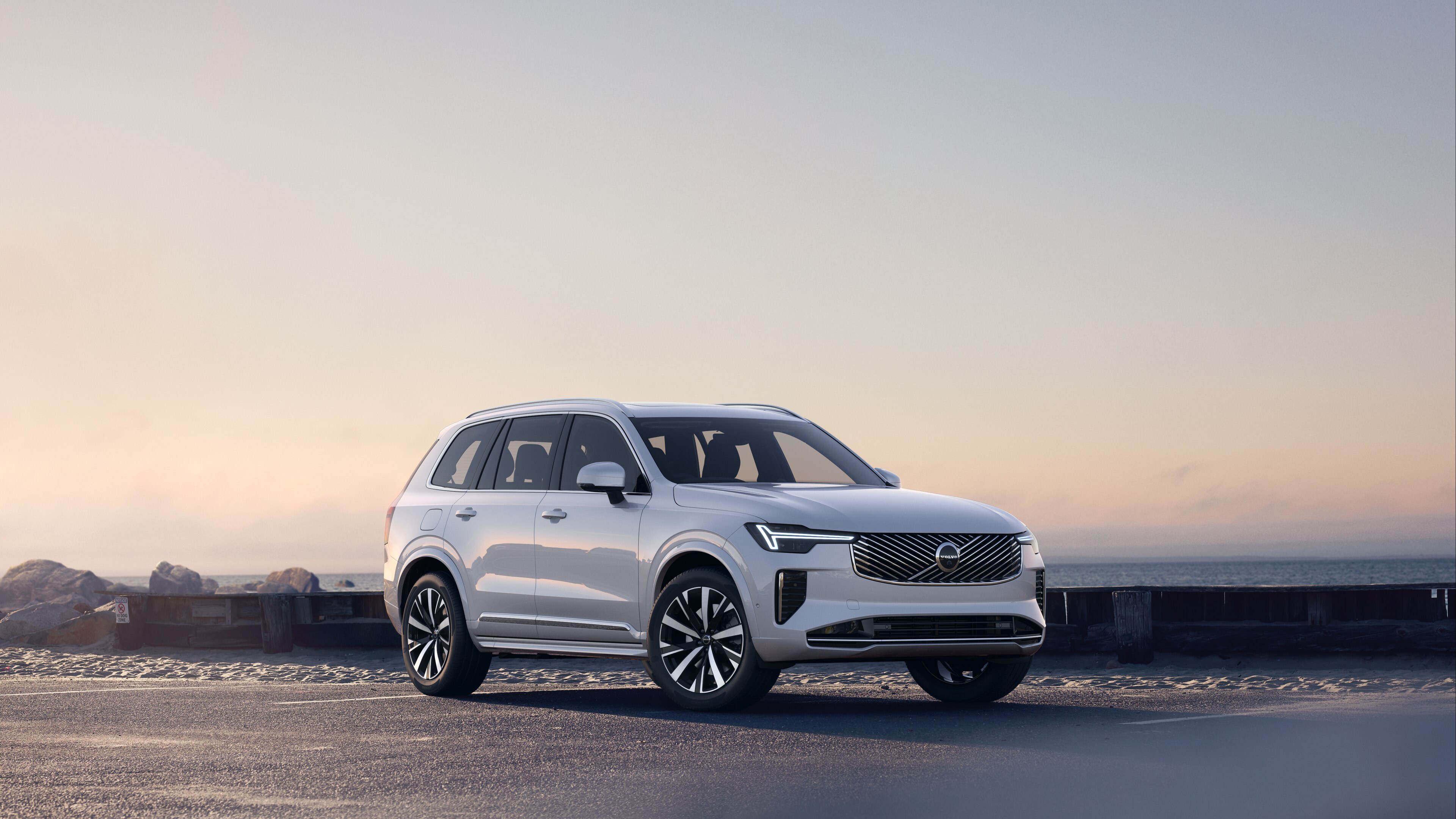 Volvo car in three-quarter view on coastal road, showing the front and side against a serene ocean background.