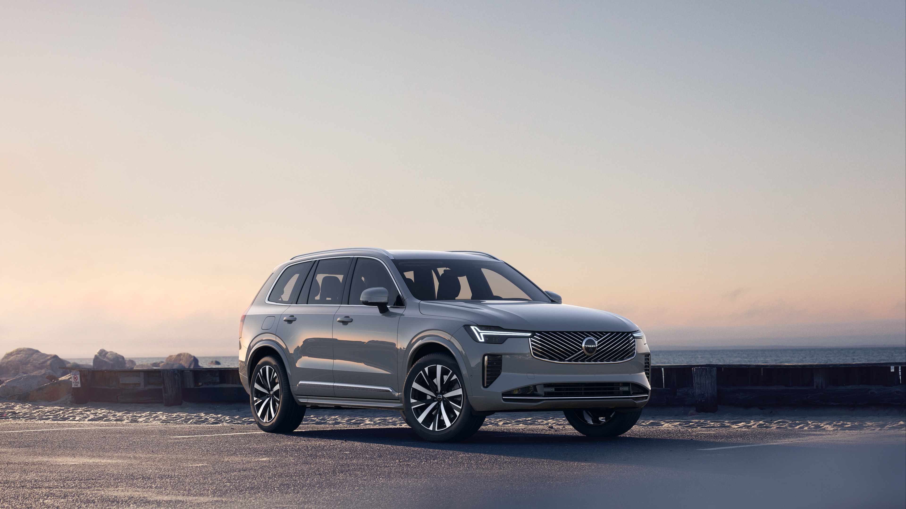 Volvo car in three-quarter view on coastal road, showing the front and side against a serene ocean background.
