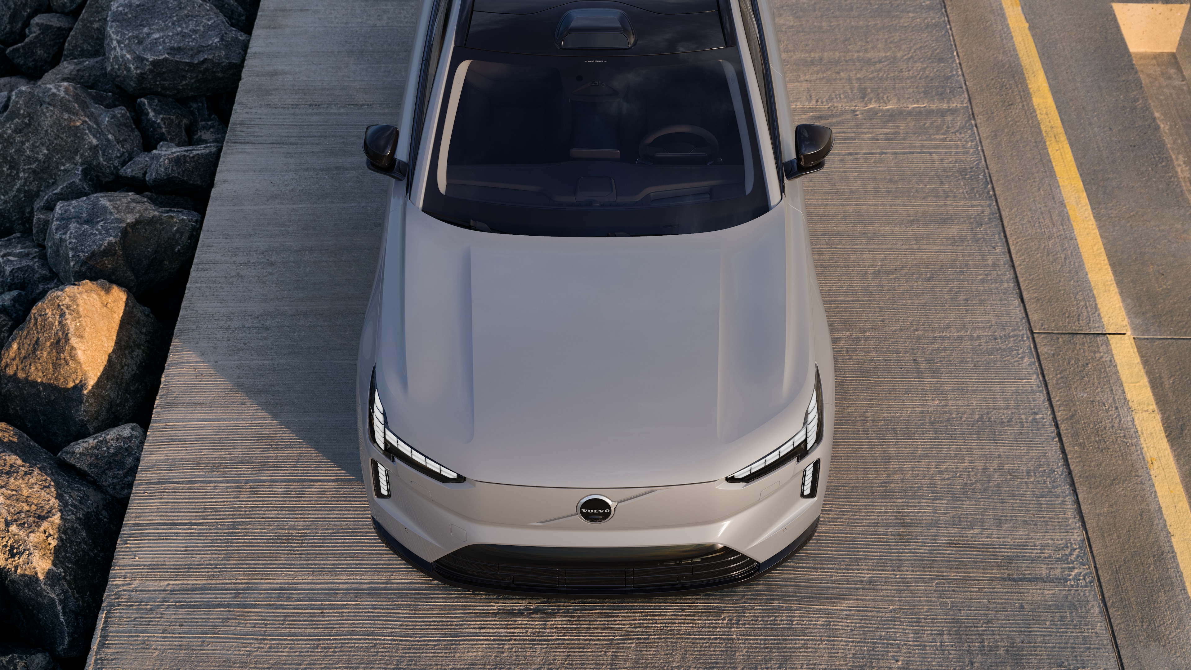 Το εξωτερικό ενός αυτοκινήτου Volvo σε άποψη τριών τετάρτων σε αστικό φόντο, όπου φαίνεται η μία πλευρά, η οροφή και μέρος του εμπρός.