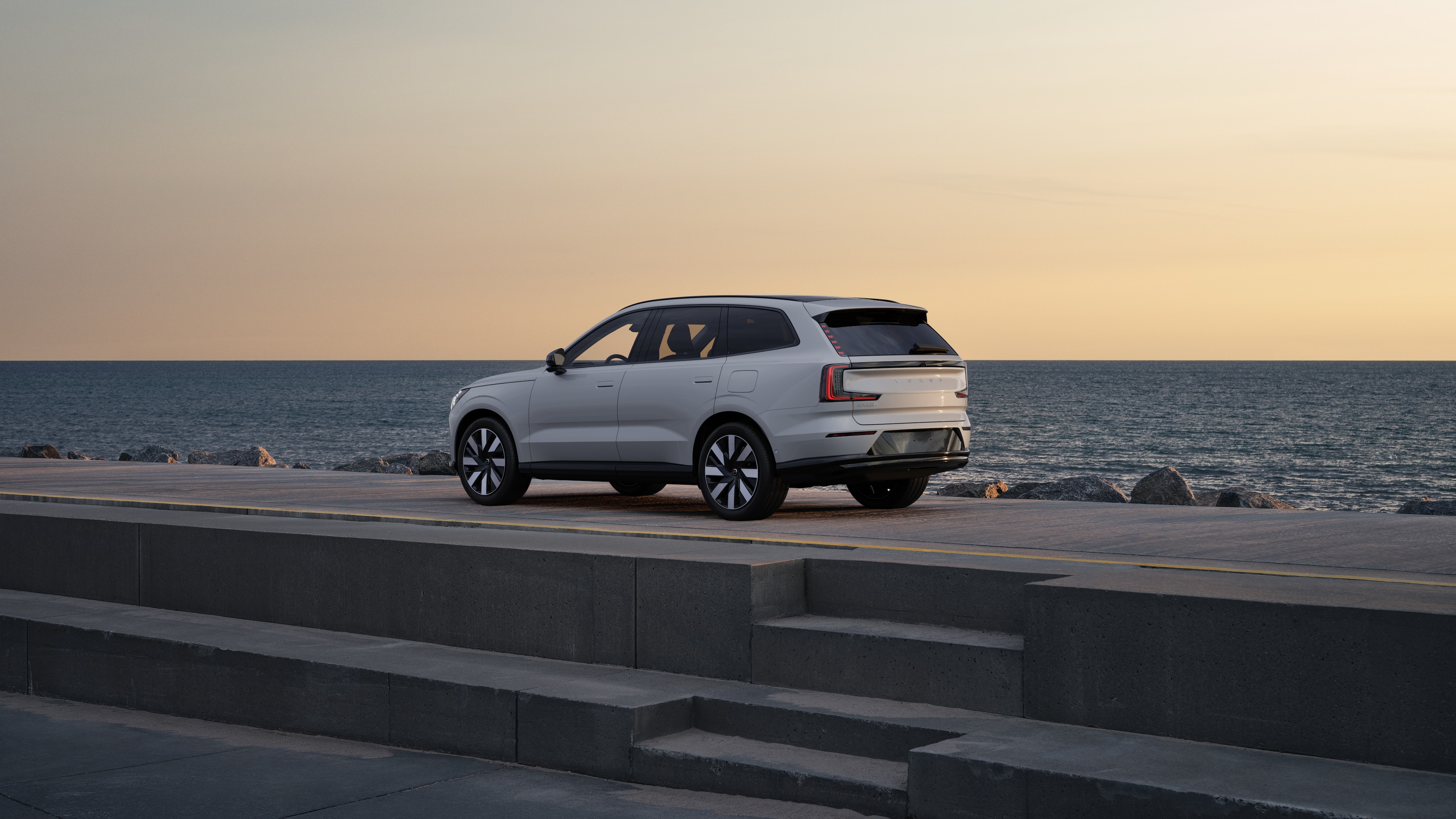 Vehículo Volvo en vista trasera de tres cuartos estacionado contra un muro de hormigón en un fondo de calle urbana.