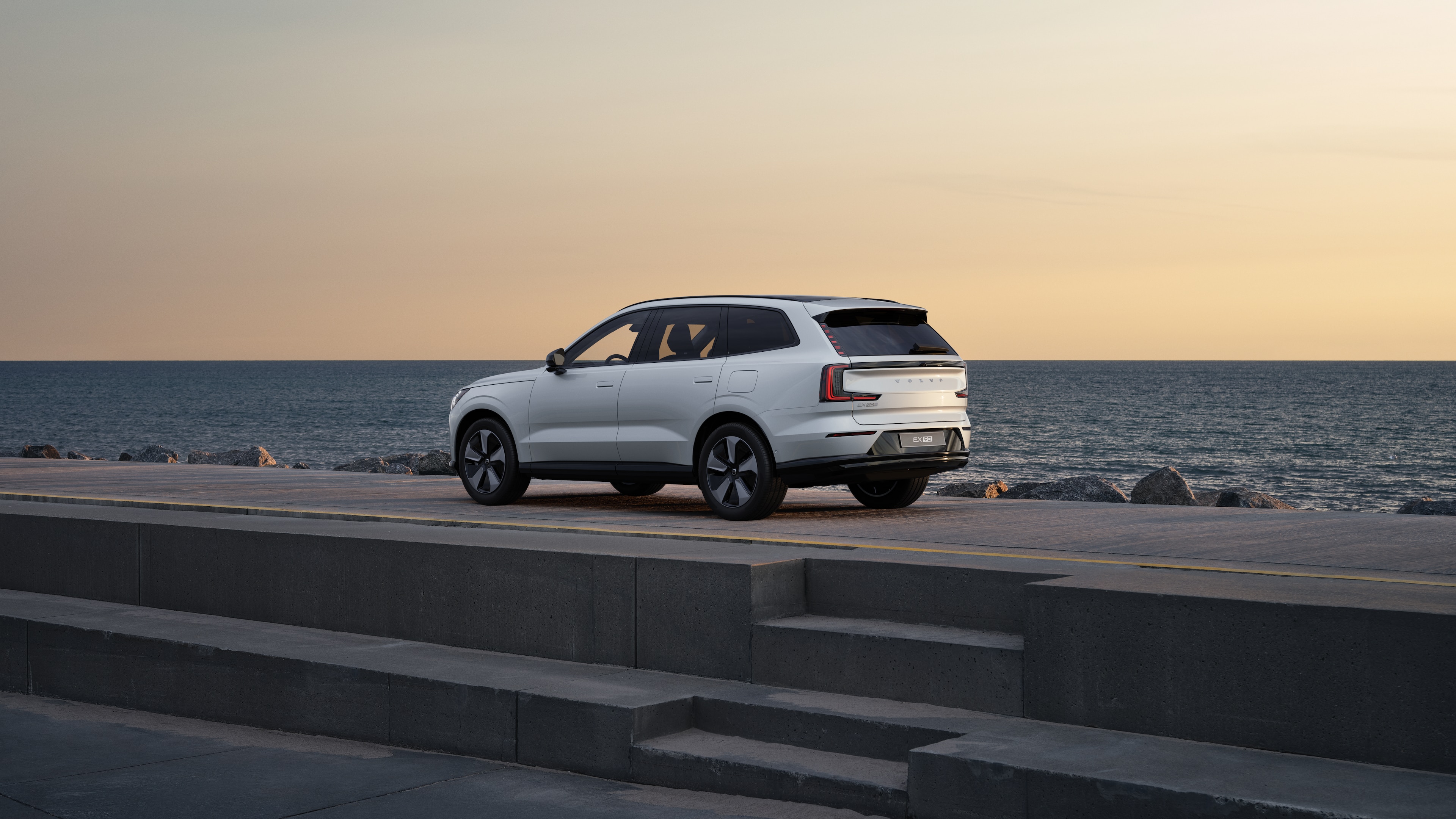Volvo car in rear three-quarter view parked against a concrete wall on an urban street background.