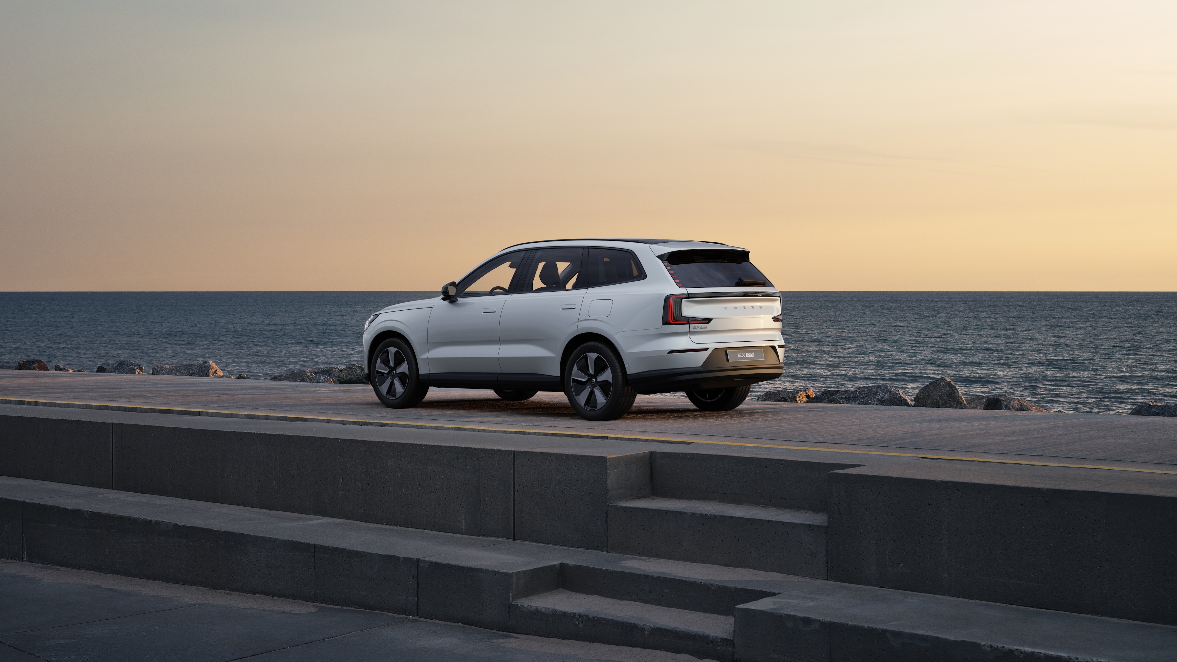 Volvo en vue arrière de trois quarts, garée contre un mur en béton dans une rue urbaine.
