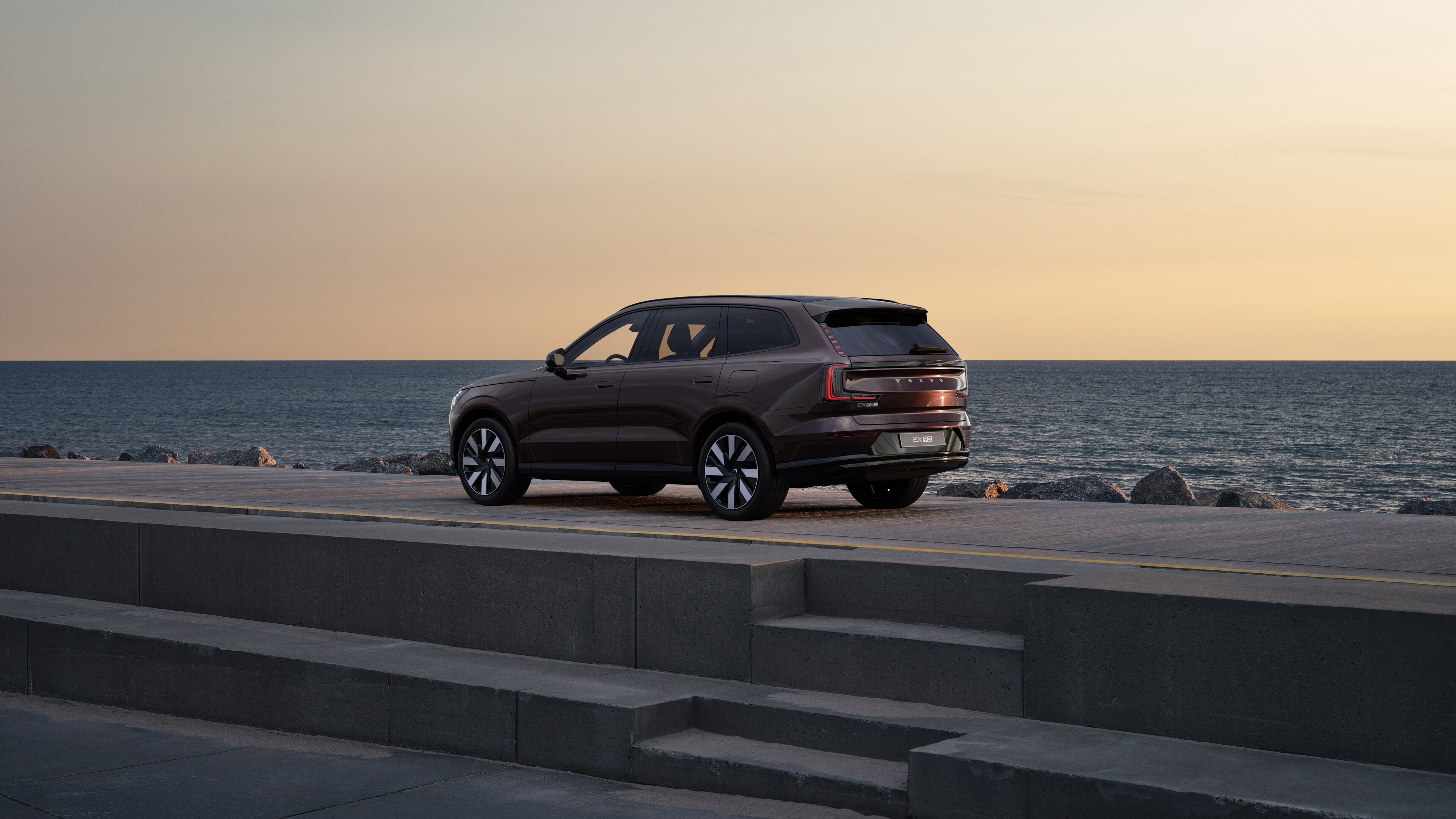 Vehículo Volvo en vista trasera de tres cuartos estacionado contra un muro de hormigón en un fondo de calle urbana.