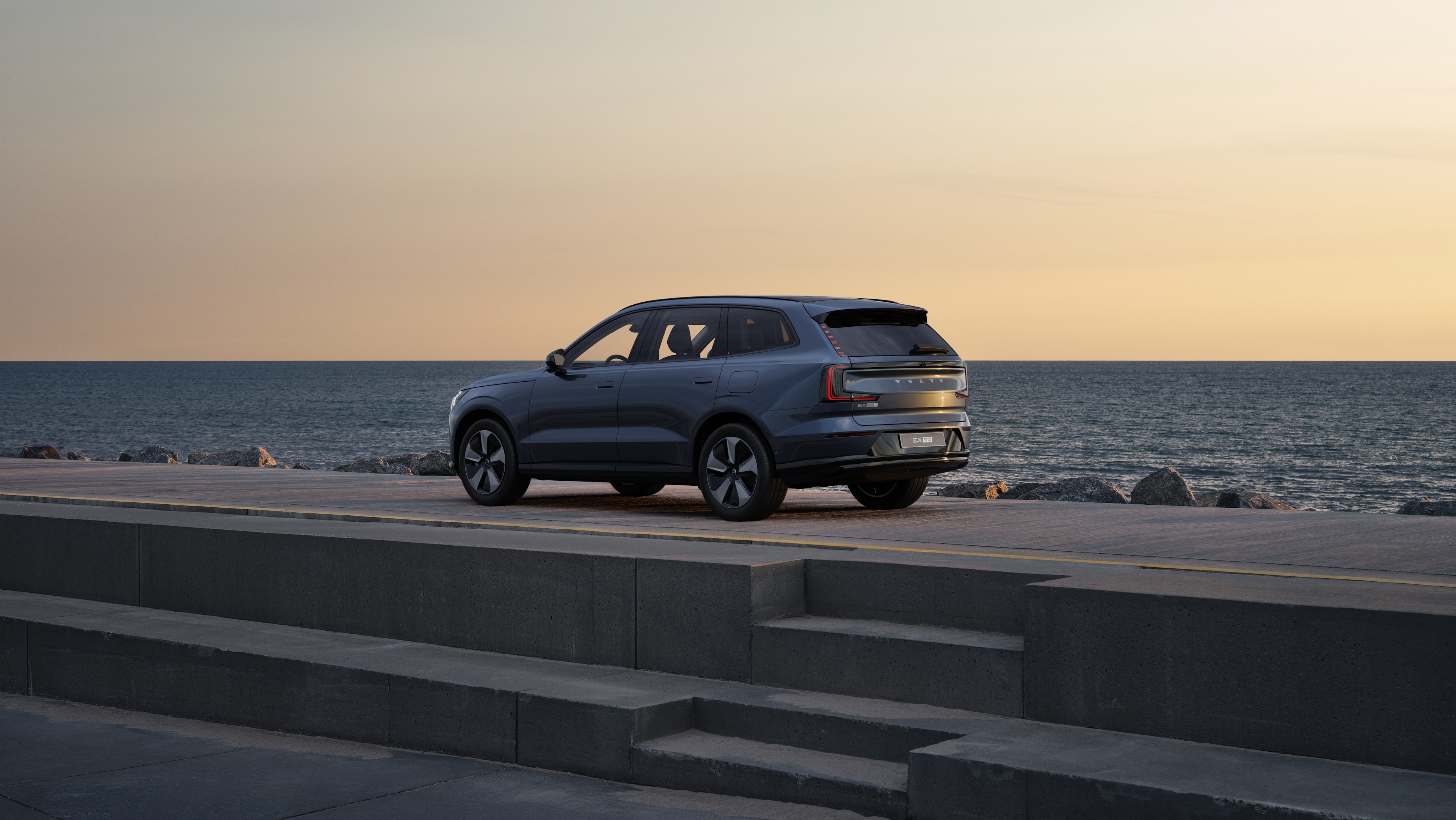 Trekvart visning av Volvo bak parkert mot en betongvegg i en urban gatebakgrunn.