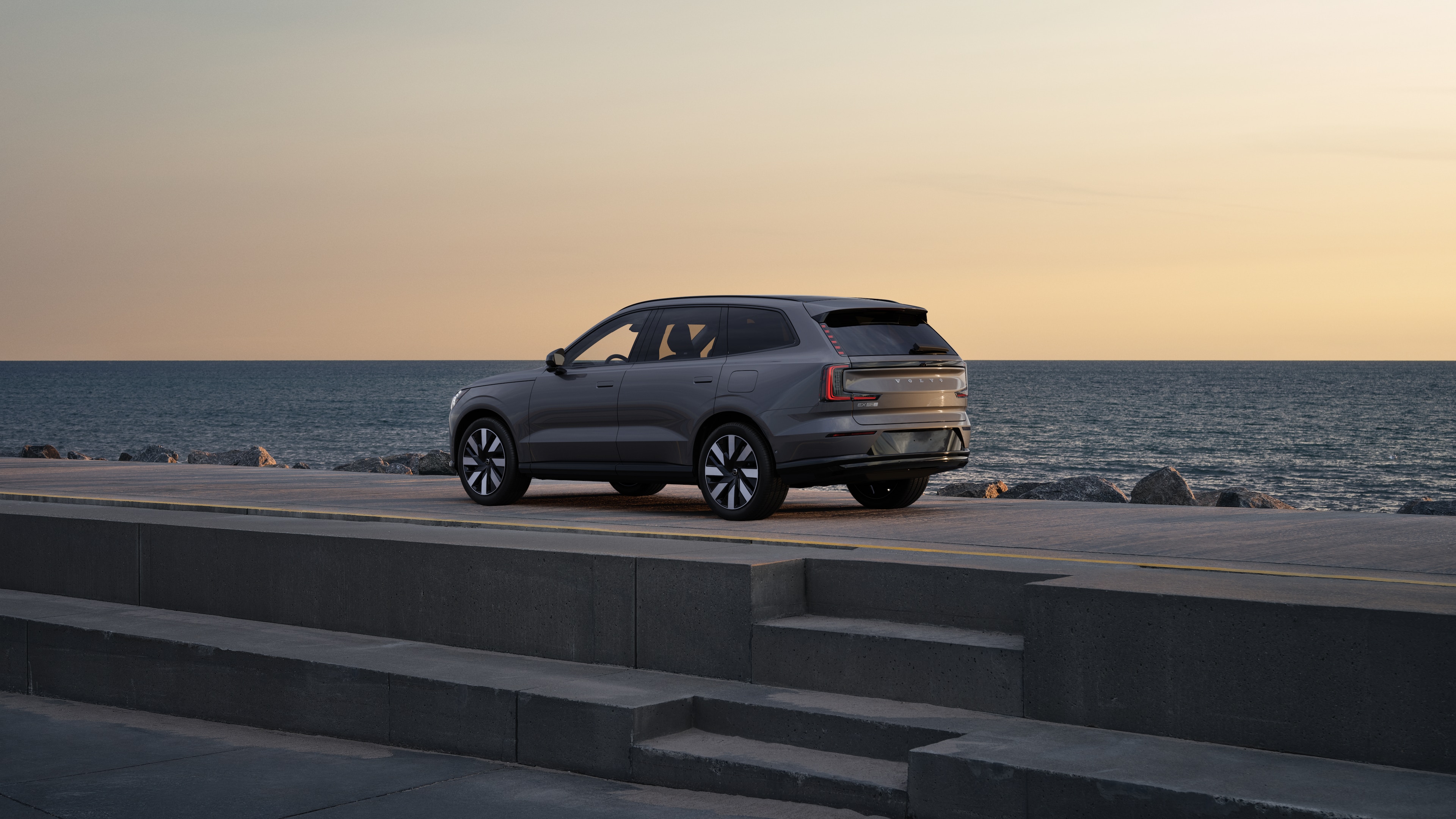 Vehículo Volvo en vista trasera de tres cuartos estacionado contra un muro de hormigón en un fondo de calle urbana.