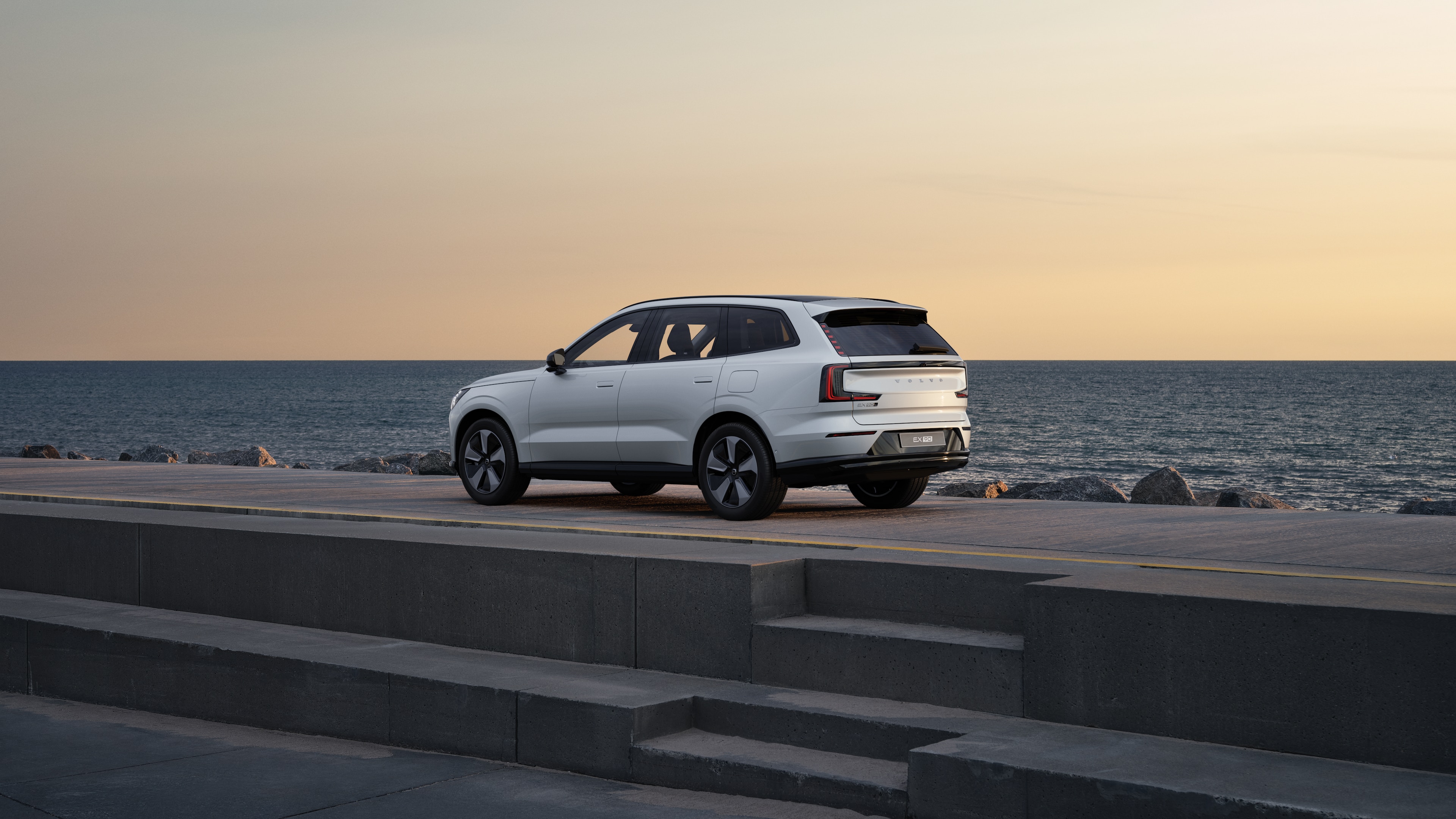 Volvo car in rear three-quarter view parked against a concrete wall on an urban street background.