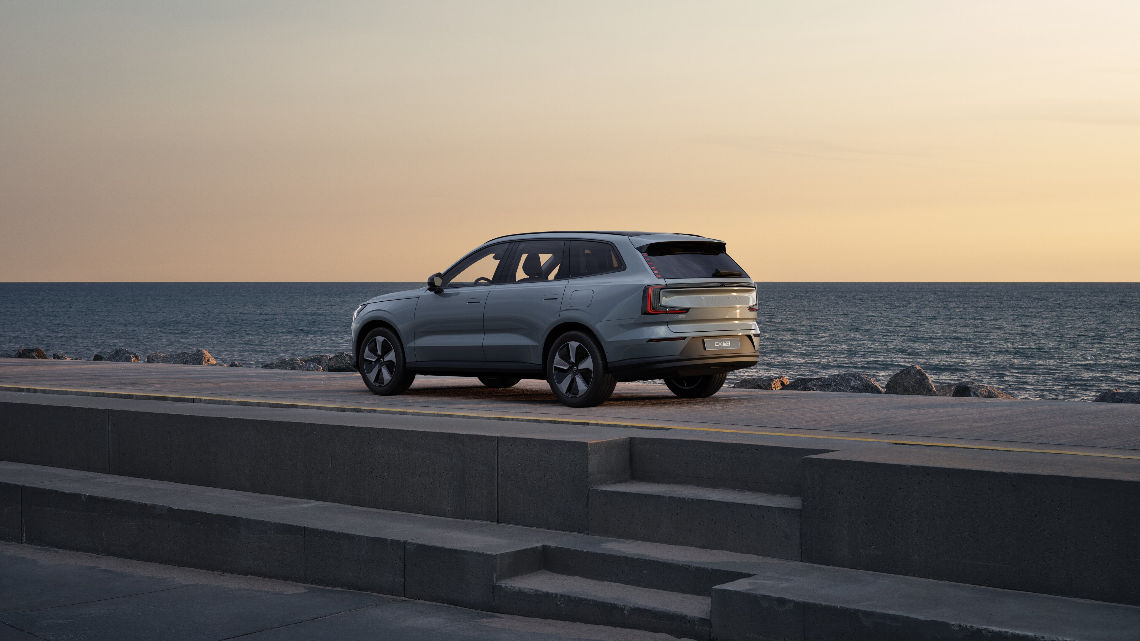 Driekwart achteraanzicht van een Volvo-auto geparkeerd tegen een betonnen muur op de achtergrond van een stedelijke straat.