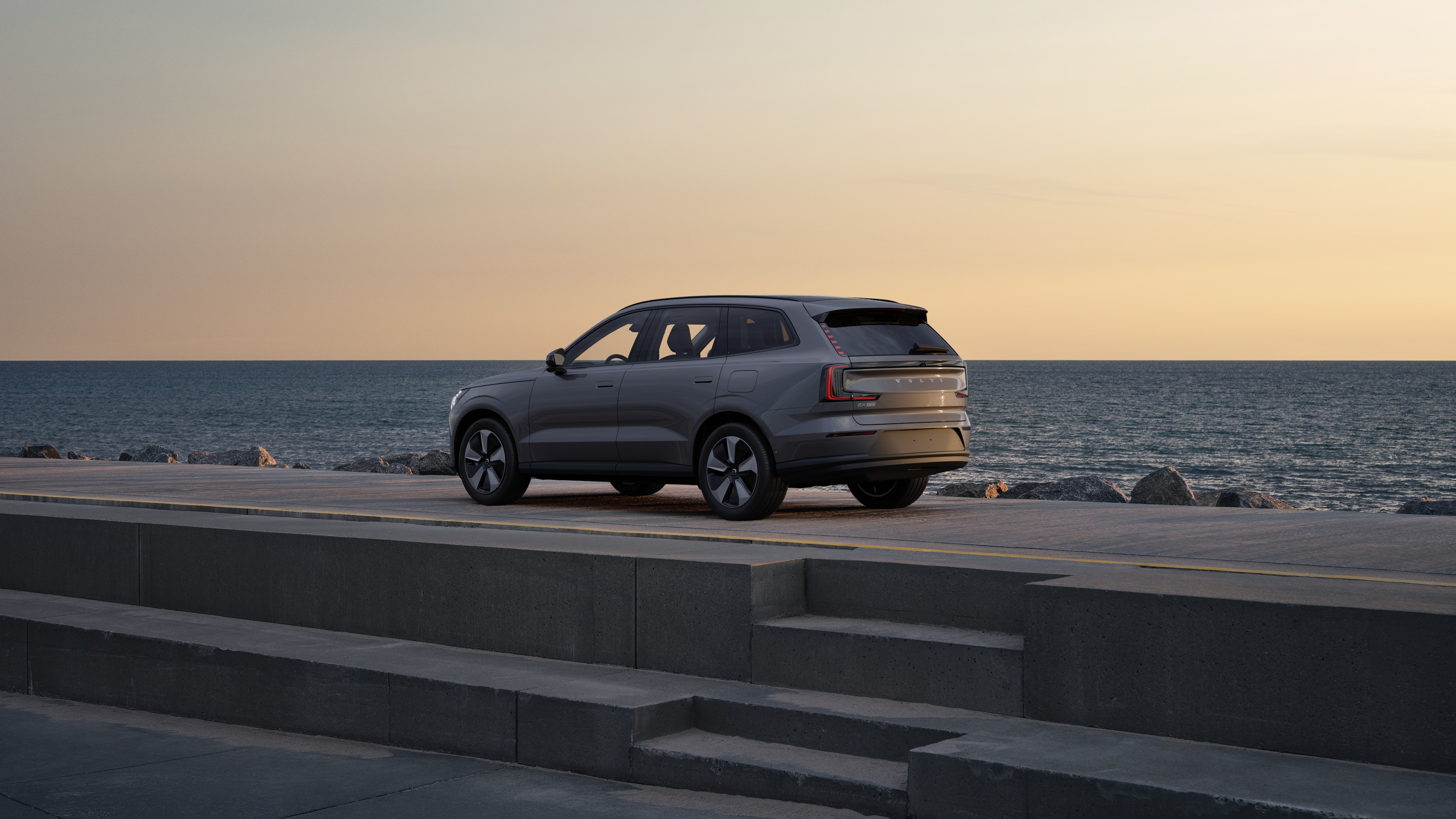 Volvo-auto in driekwart achteraanzicht geparkeerd tegen een betonnen muur op een stedelijke straatachtergrond.