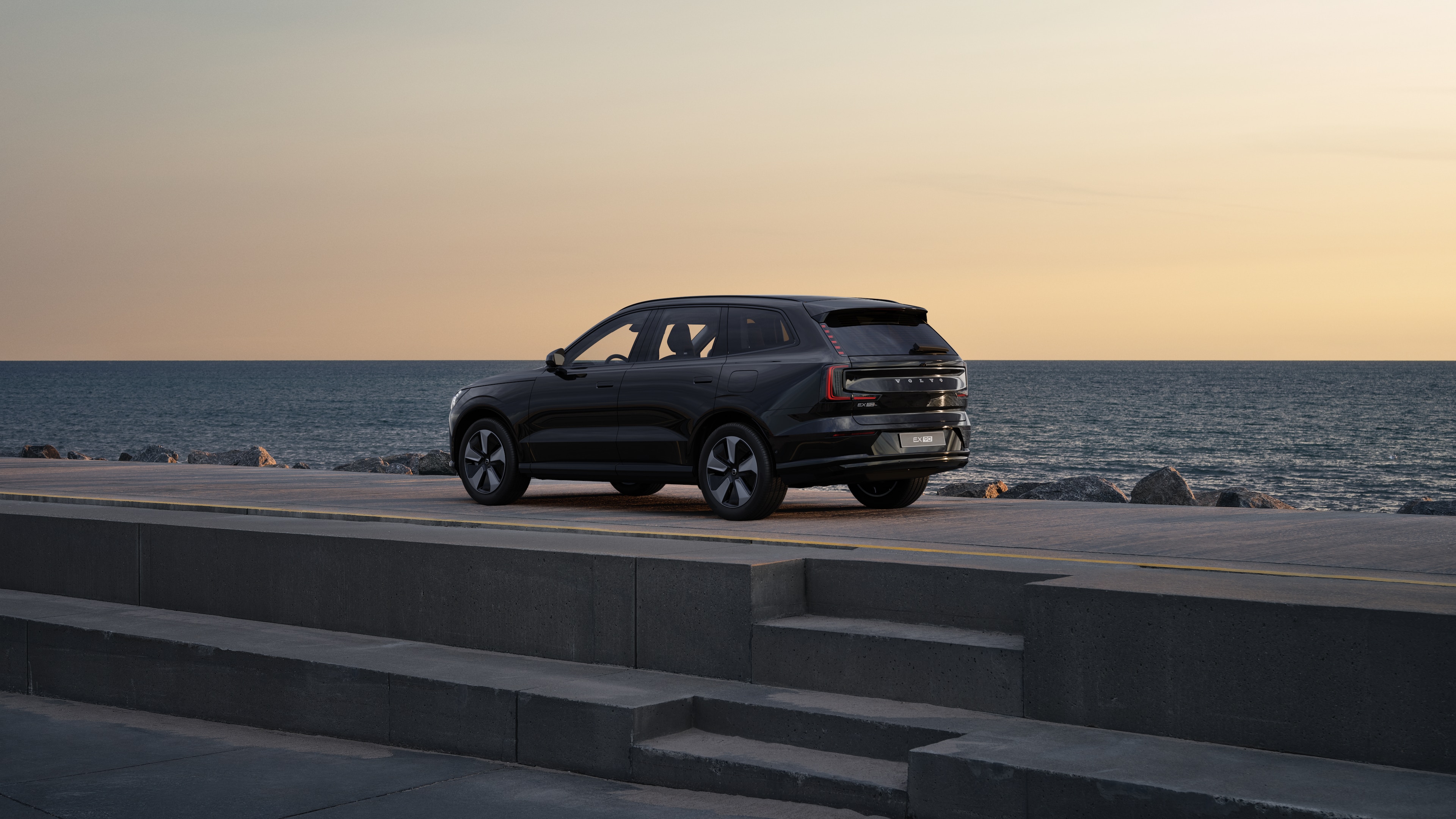 Автомобіль Volvo ззаду з видом на три чверті, припаркований біля бетонної стіни на тлі міської вулиці.