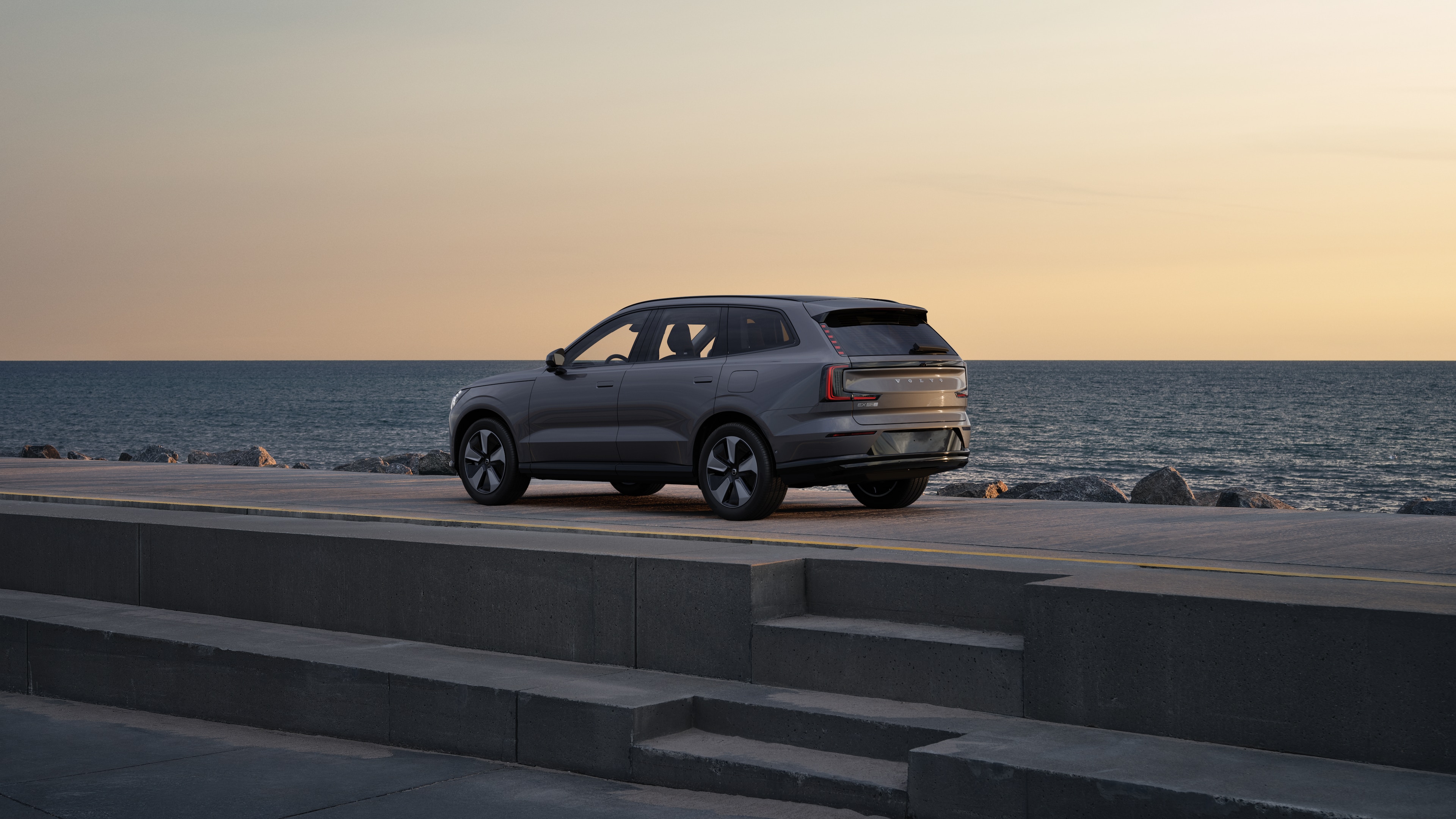 Trekvart visning av Volvo bak parkert mot en betongvegg i en urban gatebakgrunn.
