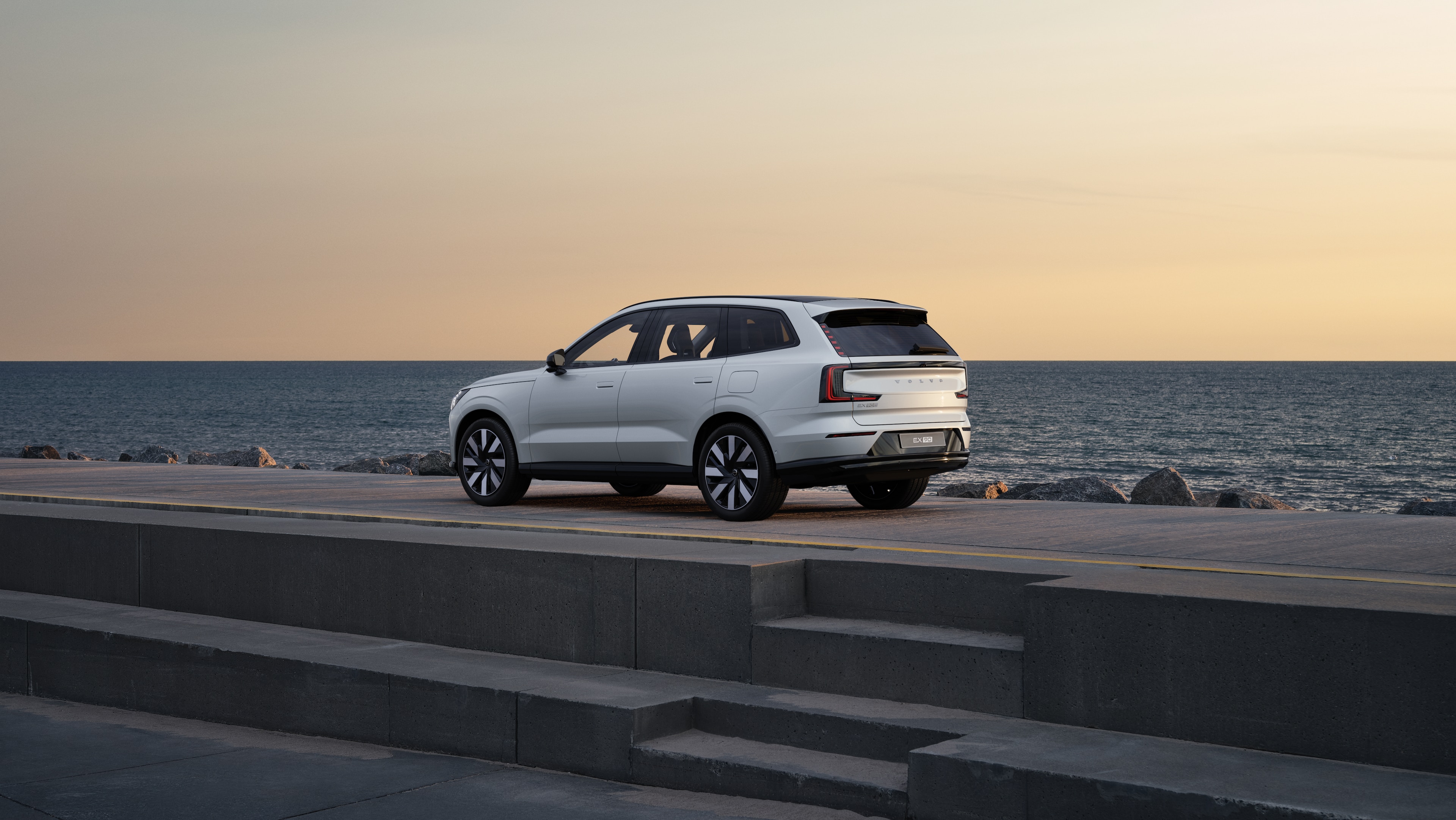 Volvo car in rear three-quarter view parked against a concrete wall on an urban street background.