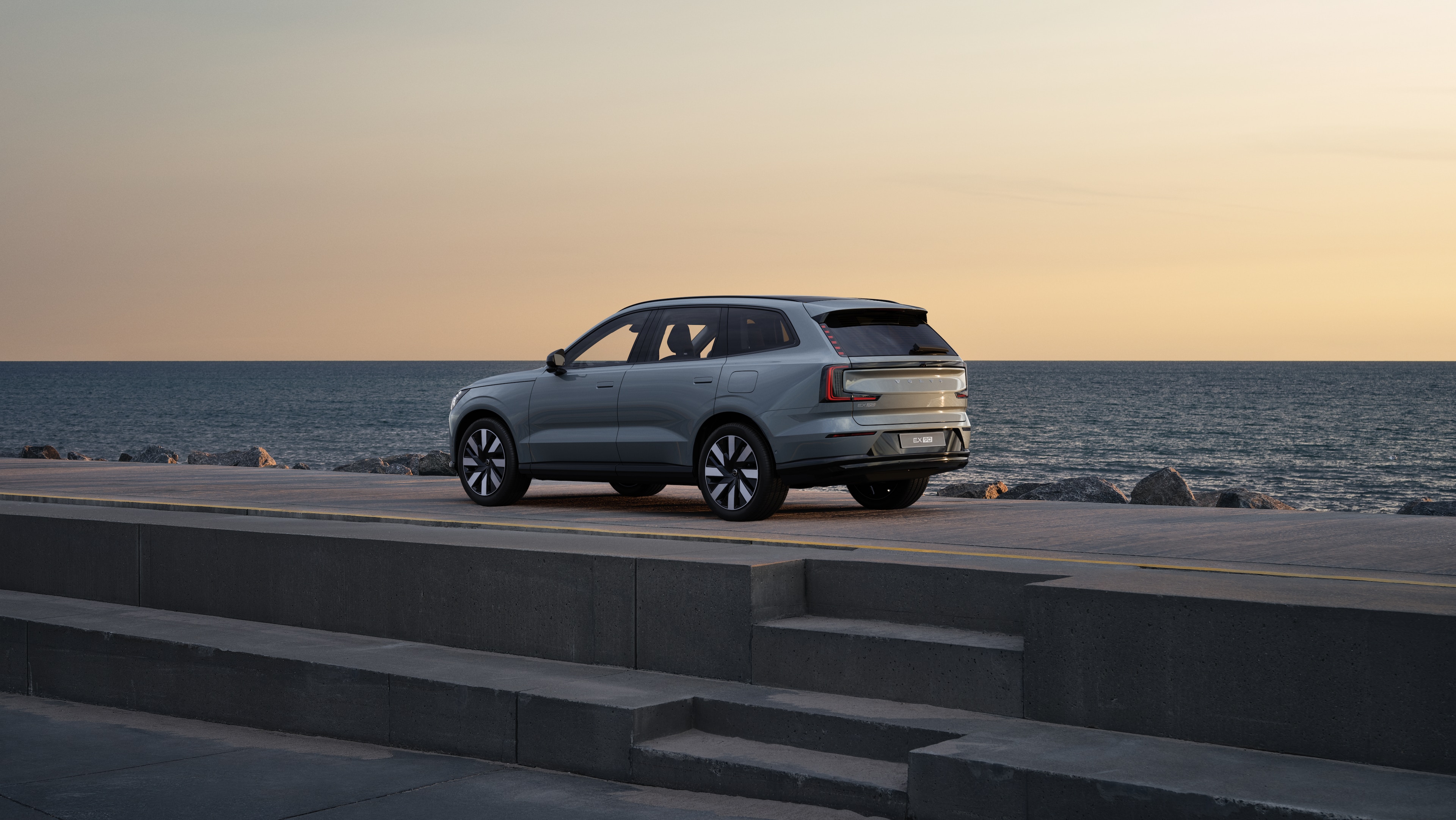 Volvo car in rear three-quarter view parked against a concrete wall on an urban street background.