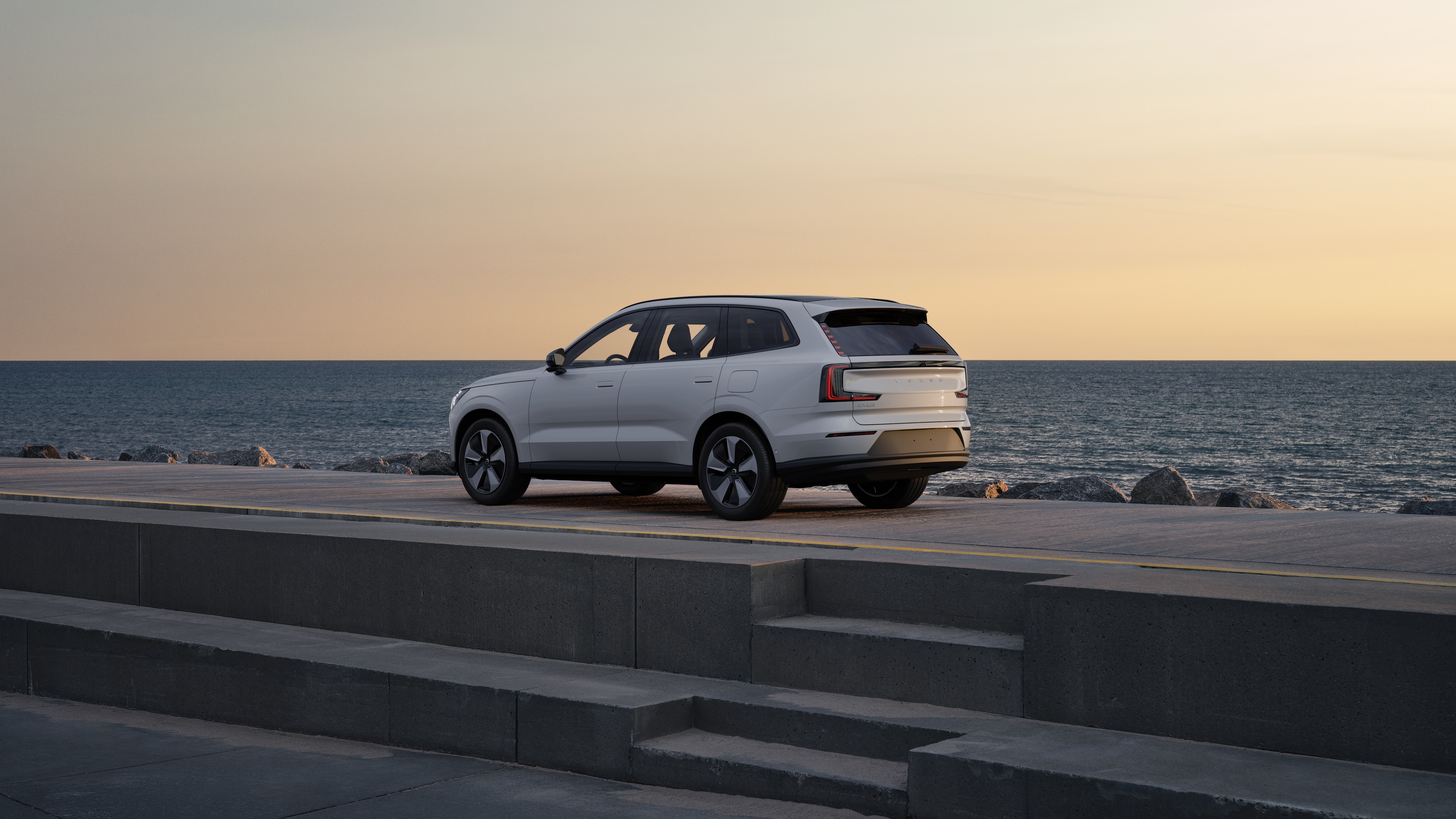 Volvo-auto in driekwart achteraanzicht geparkeerd tegen een betonnen muur op een stedelijke straatachtergrond.