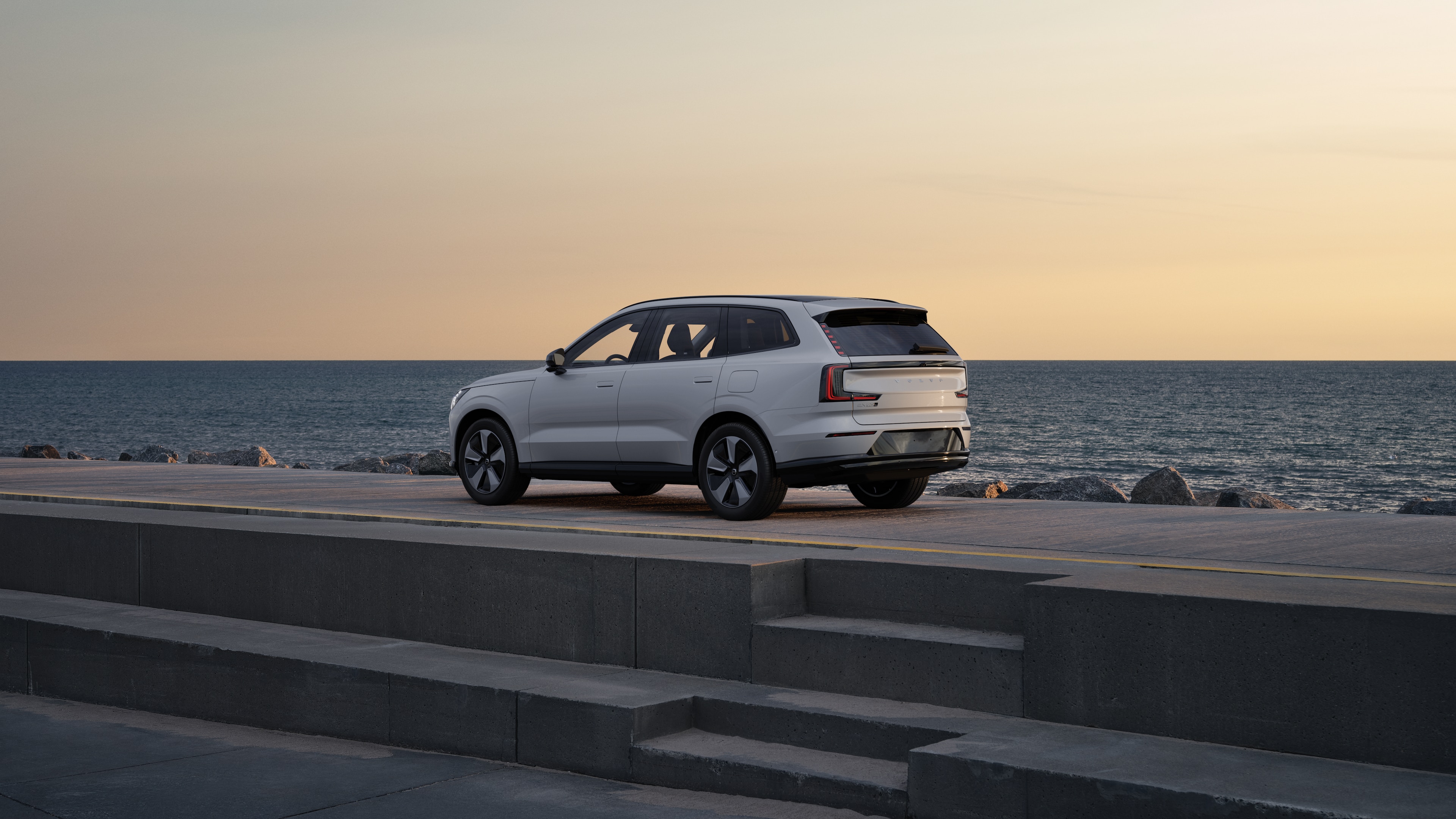 Автомобил Volvo отзад с изглед от три четвърти, паркиран до бетонна стена на фона на градска улица.