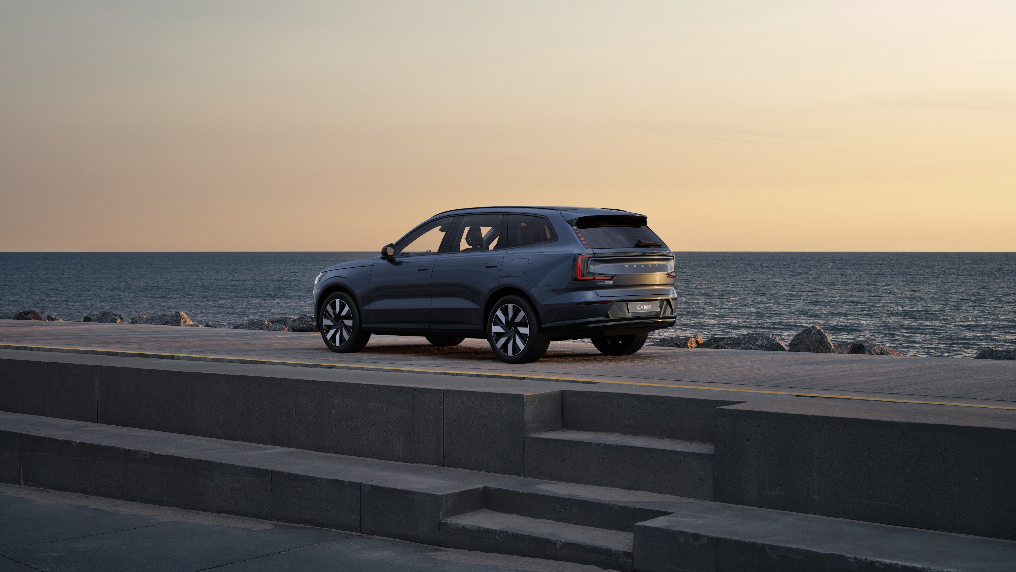 Volvo car in rear three-quarter view parked against a concrete wall on an urban street background.