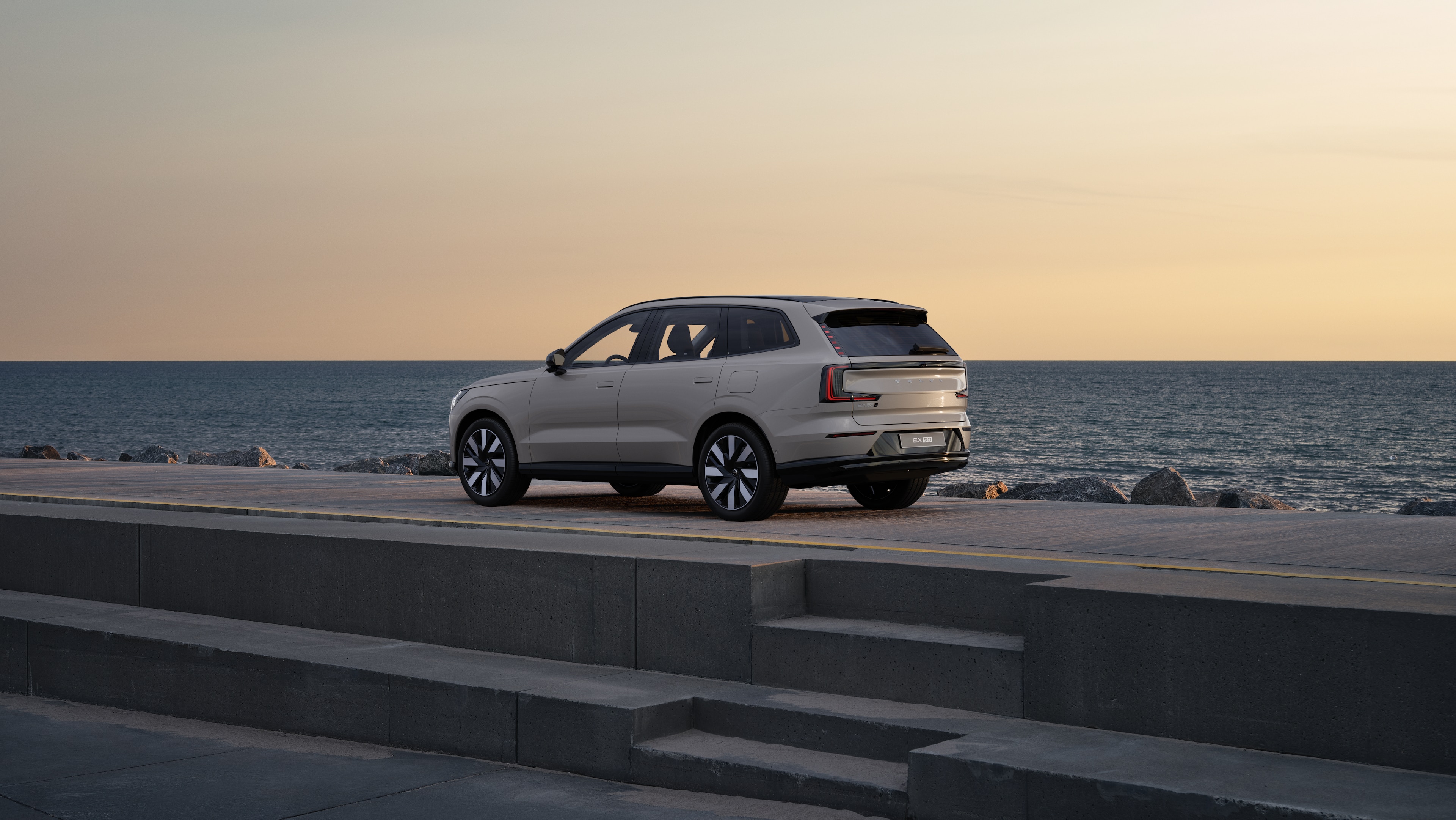 Vehículo Volvo en vista trasera de tres cuartos estacionado contra un muro de hormigón en un fondo de calle urbana.