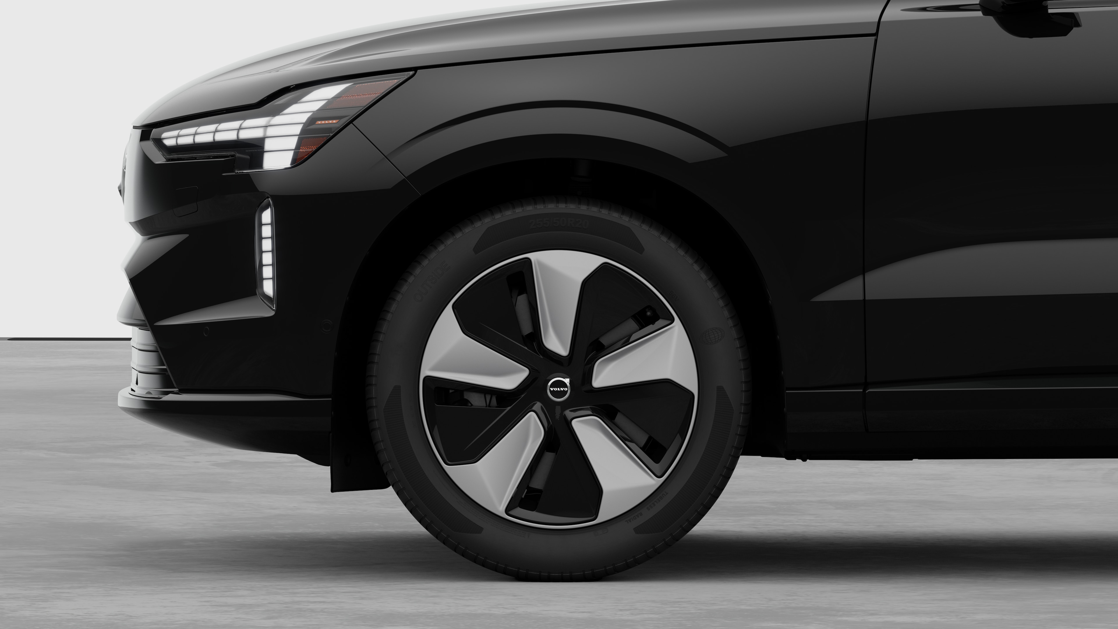 Vista lateral exterior del vehículo Volvo centrada en la rueda delantera y el guardabarros, sobre un fondo de estudio liso.
