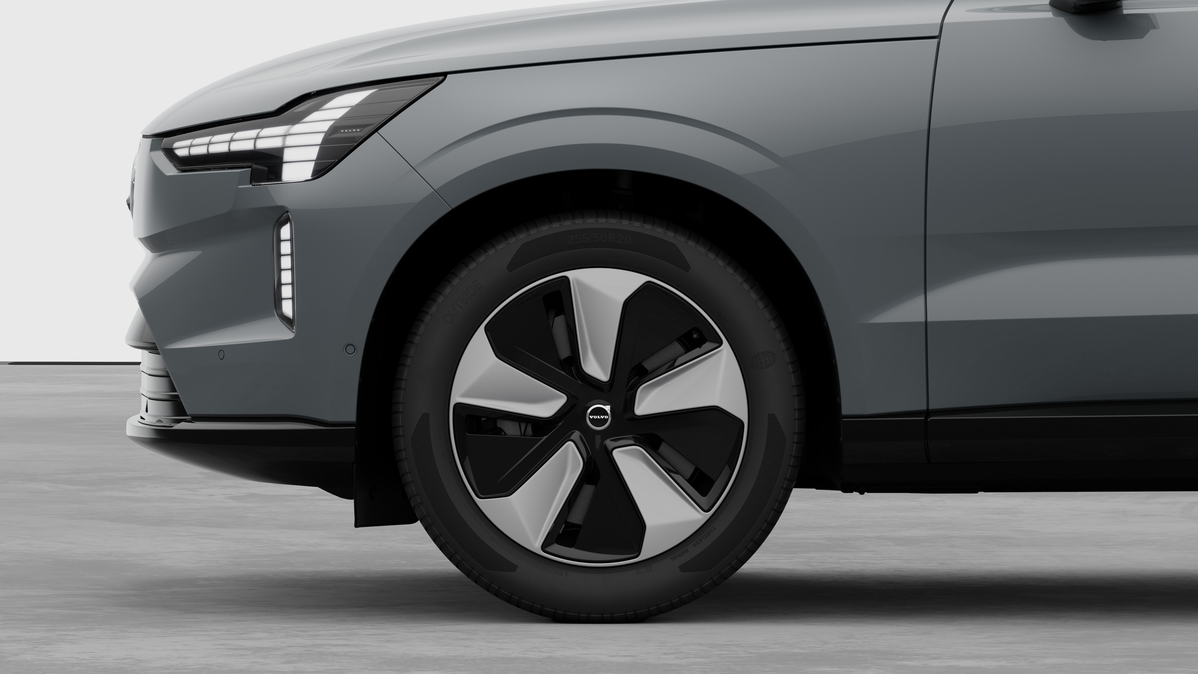 Екстериорен страничен изглед на автомобил Volvo, фокусиран върху предното колело и калника, поставен на обикновен студиен фон.