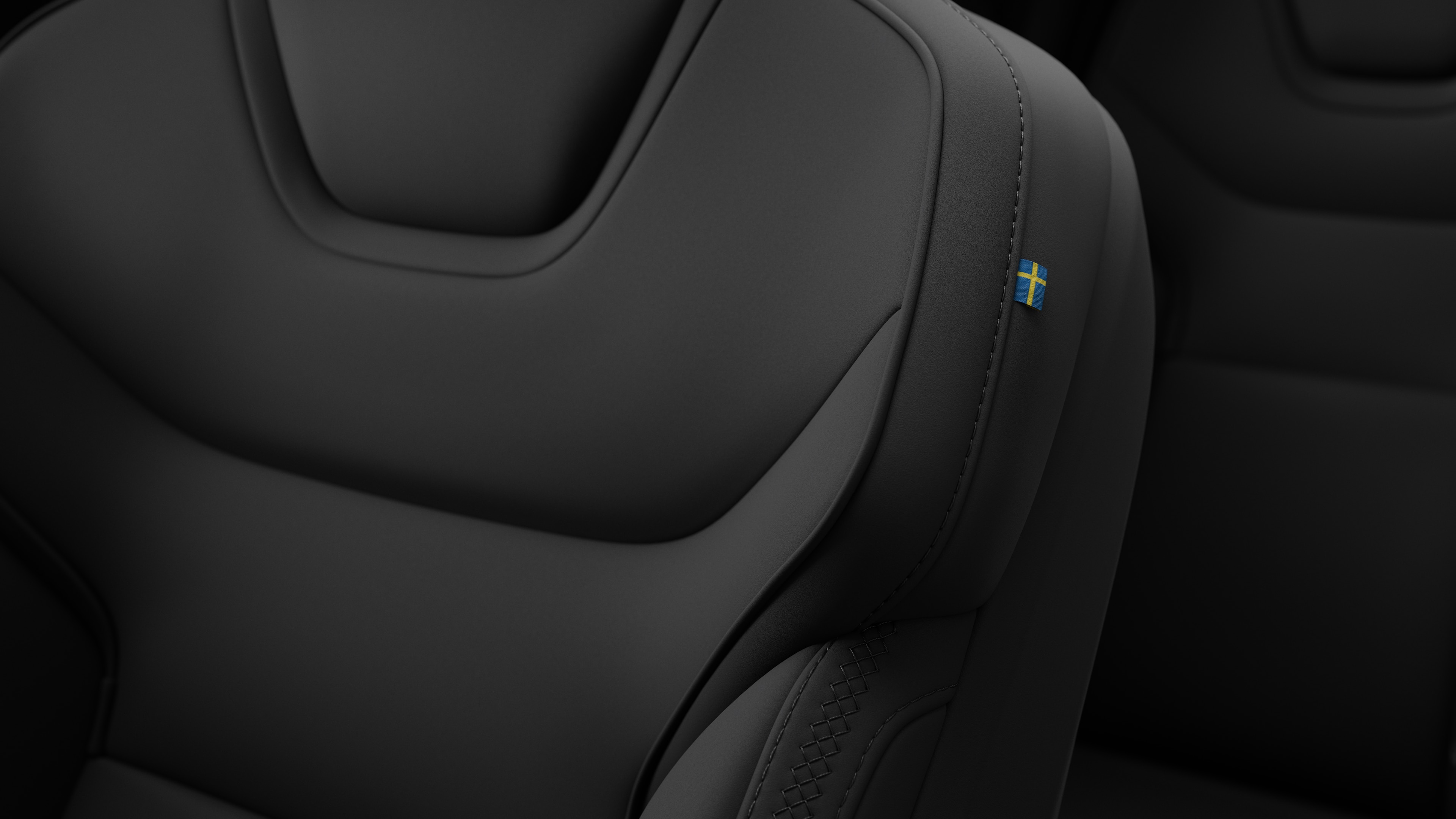 Zbliżenie na detale foteli we wnętrzu samochodu Volvo z widocznymi przeszyciami i małą plakietką z flagą szwedzką