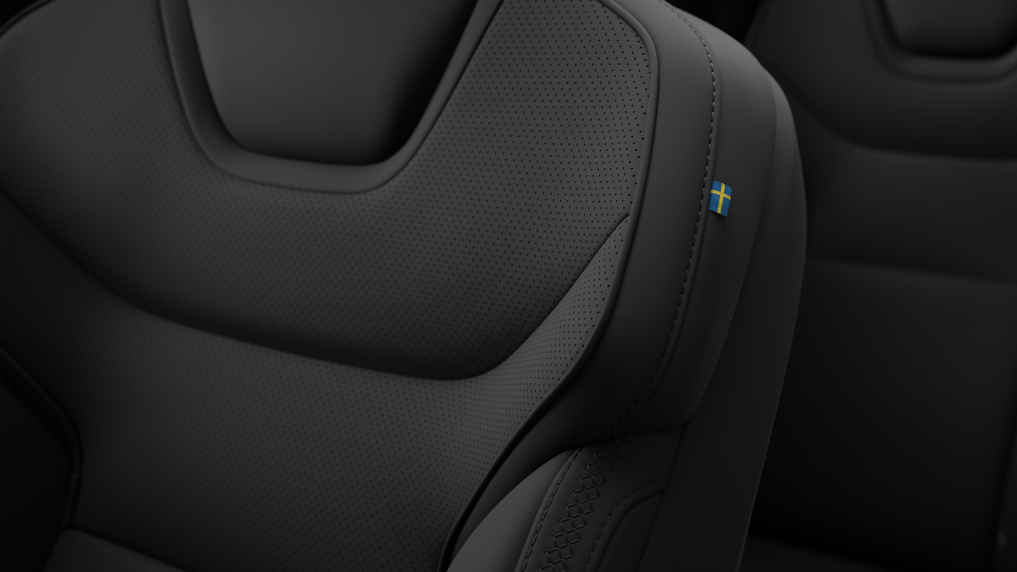 Close-up do detalhe do banco do interior do carro Volvo mostrando costuras e uma pequena etiqueta de bandeira sueca.