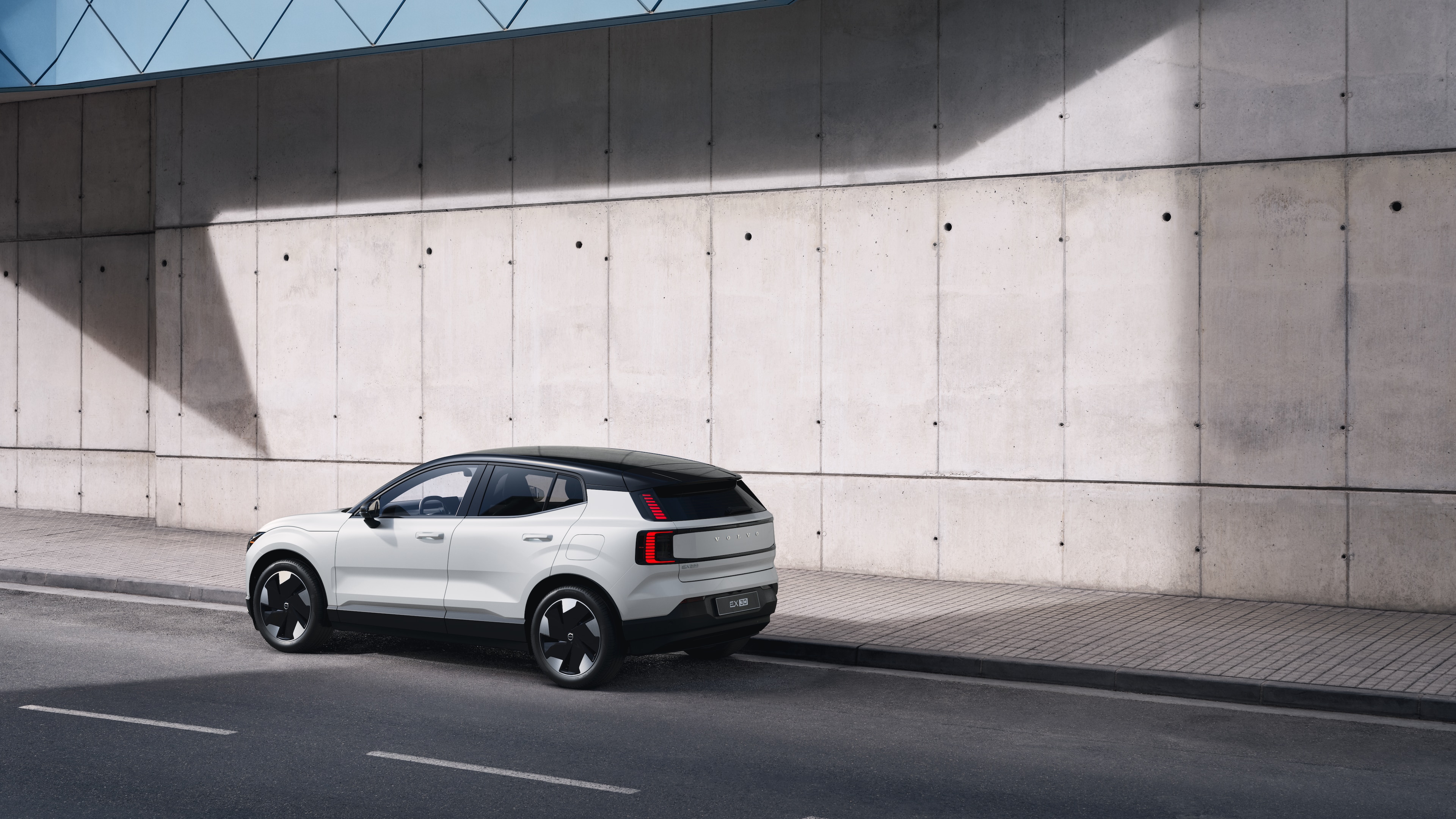 Volvo car in rear three-quarter view parked against a concrete wall on an urban street background.