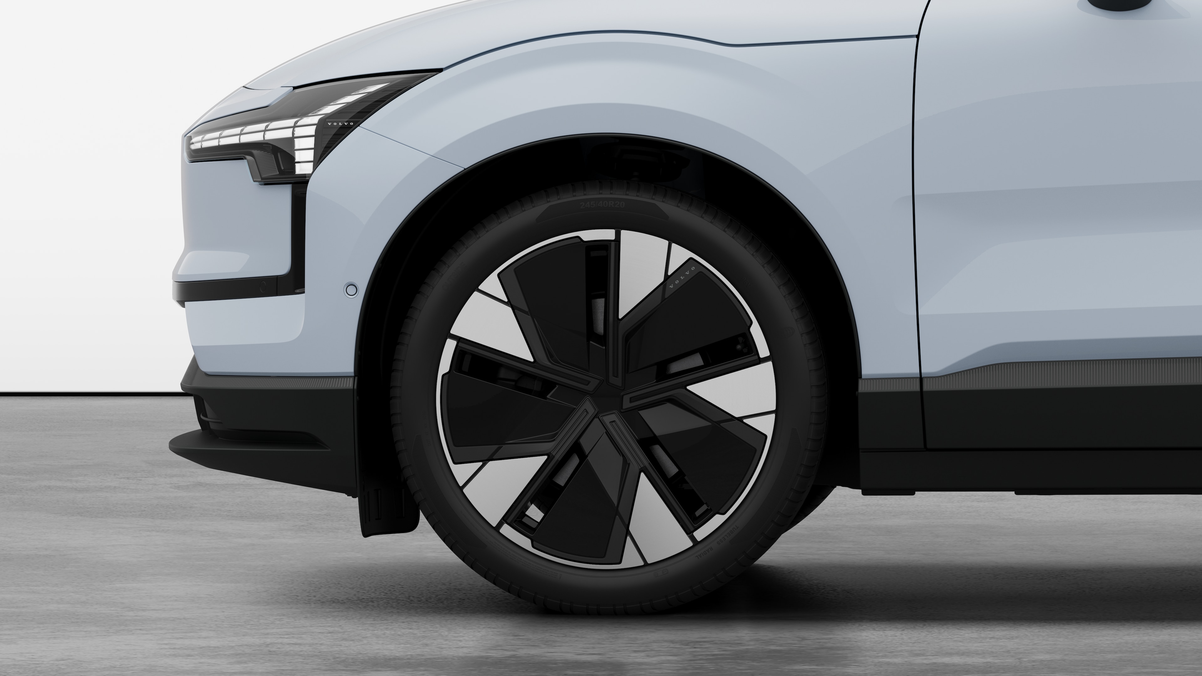 Vista lateral externa do carro Volvo com foco na roda dianteira e no para-lama, em um plano de fundo de estúdio.