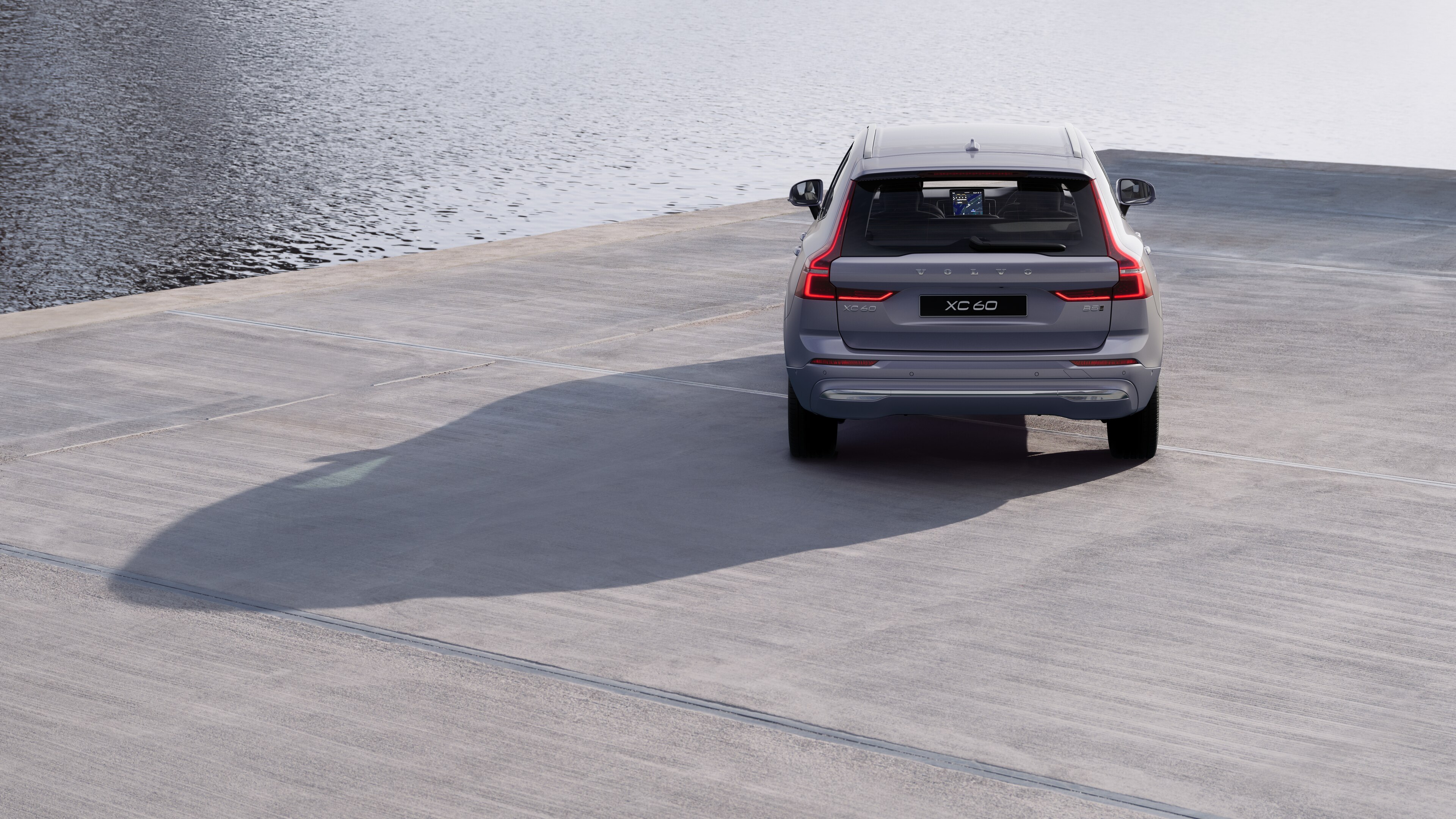 Volvo car rear view on a winding coastal road with a beachside background.