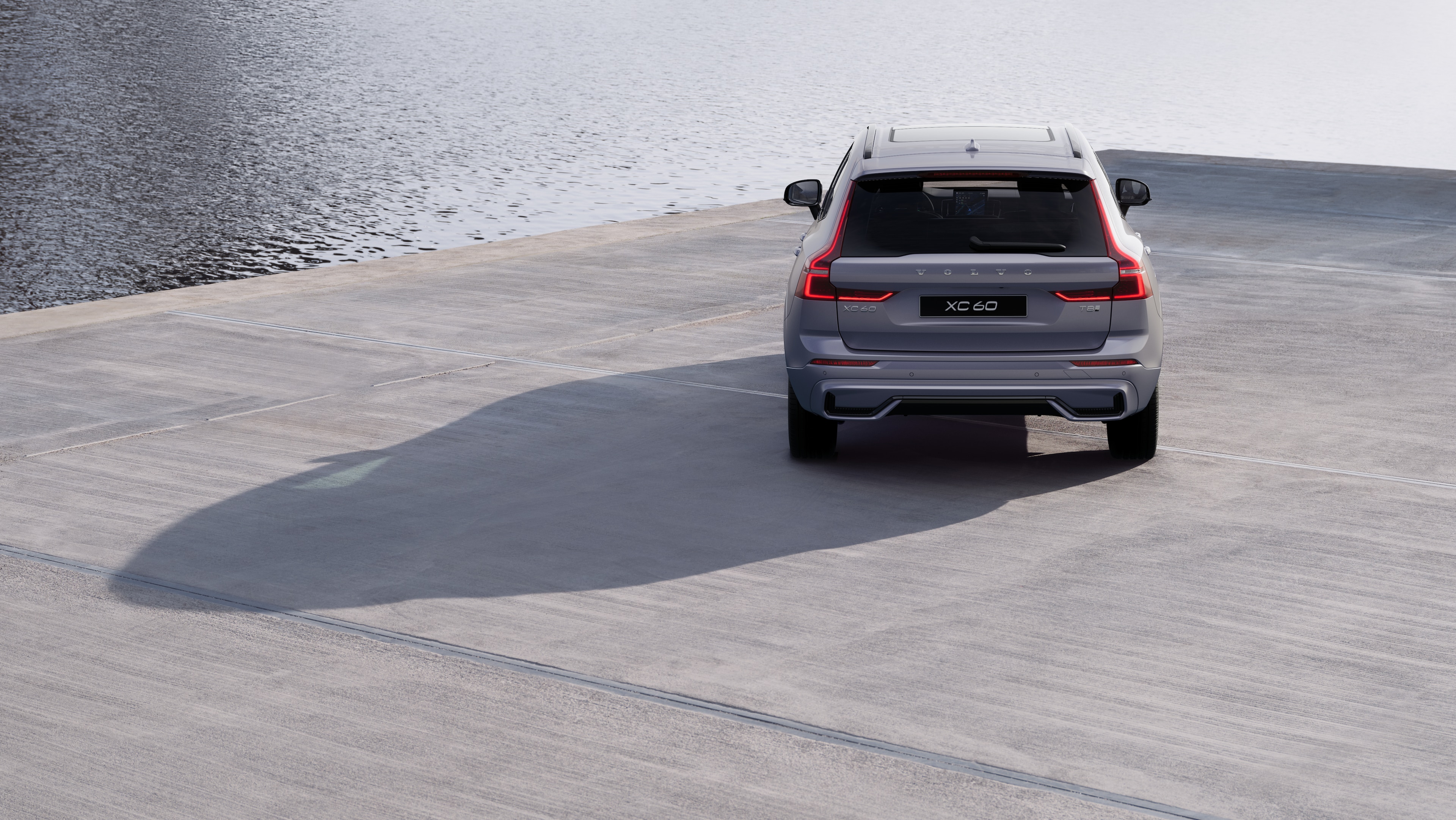 Volvo car rear view on a winding coastal road with a beachside background.