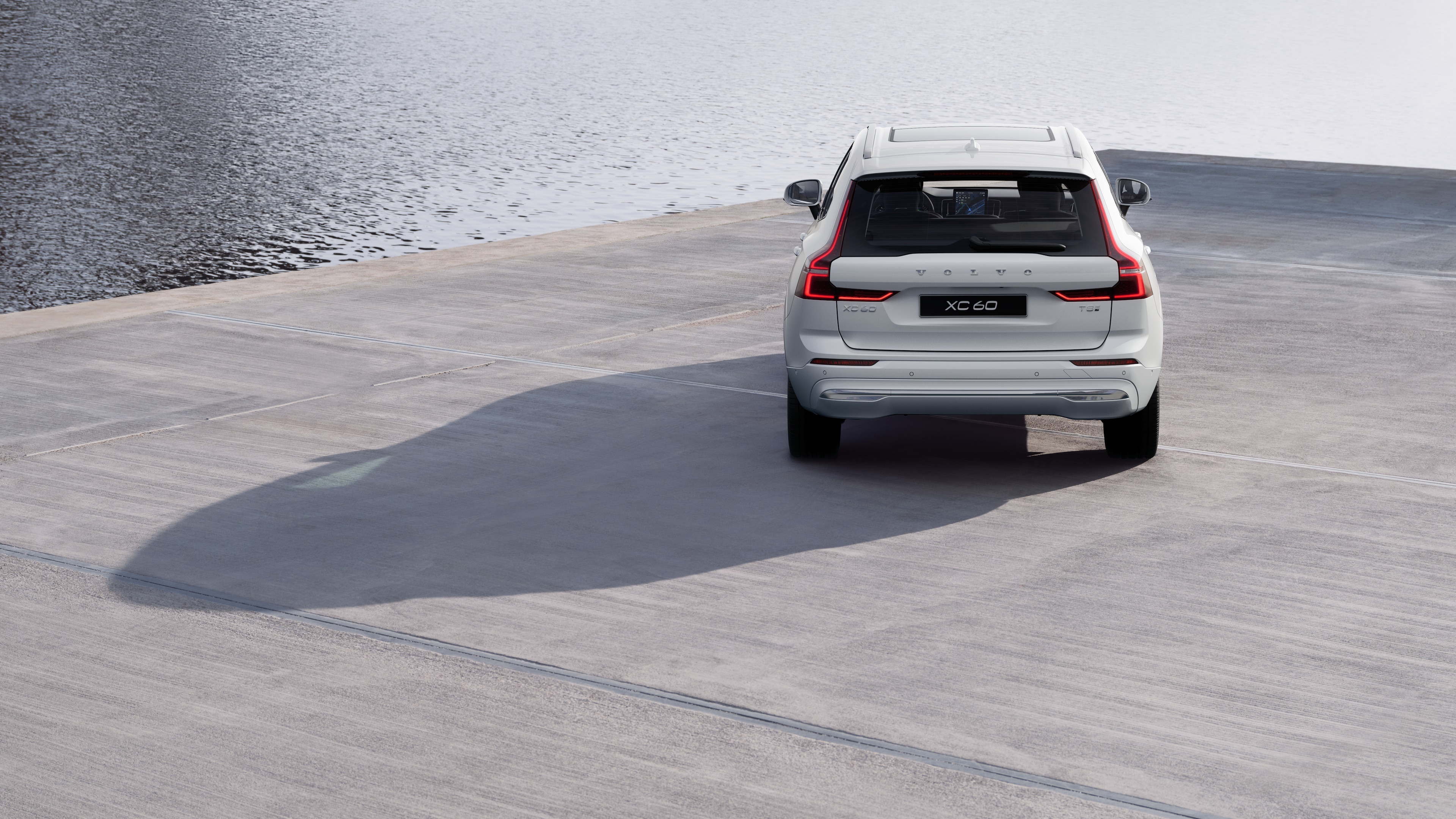 Horft aftan á Volvo-bíl á bugðóttum strandvegi með bakgrunn við ströndina.
