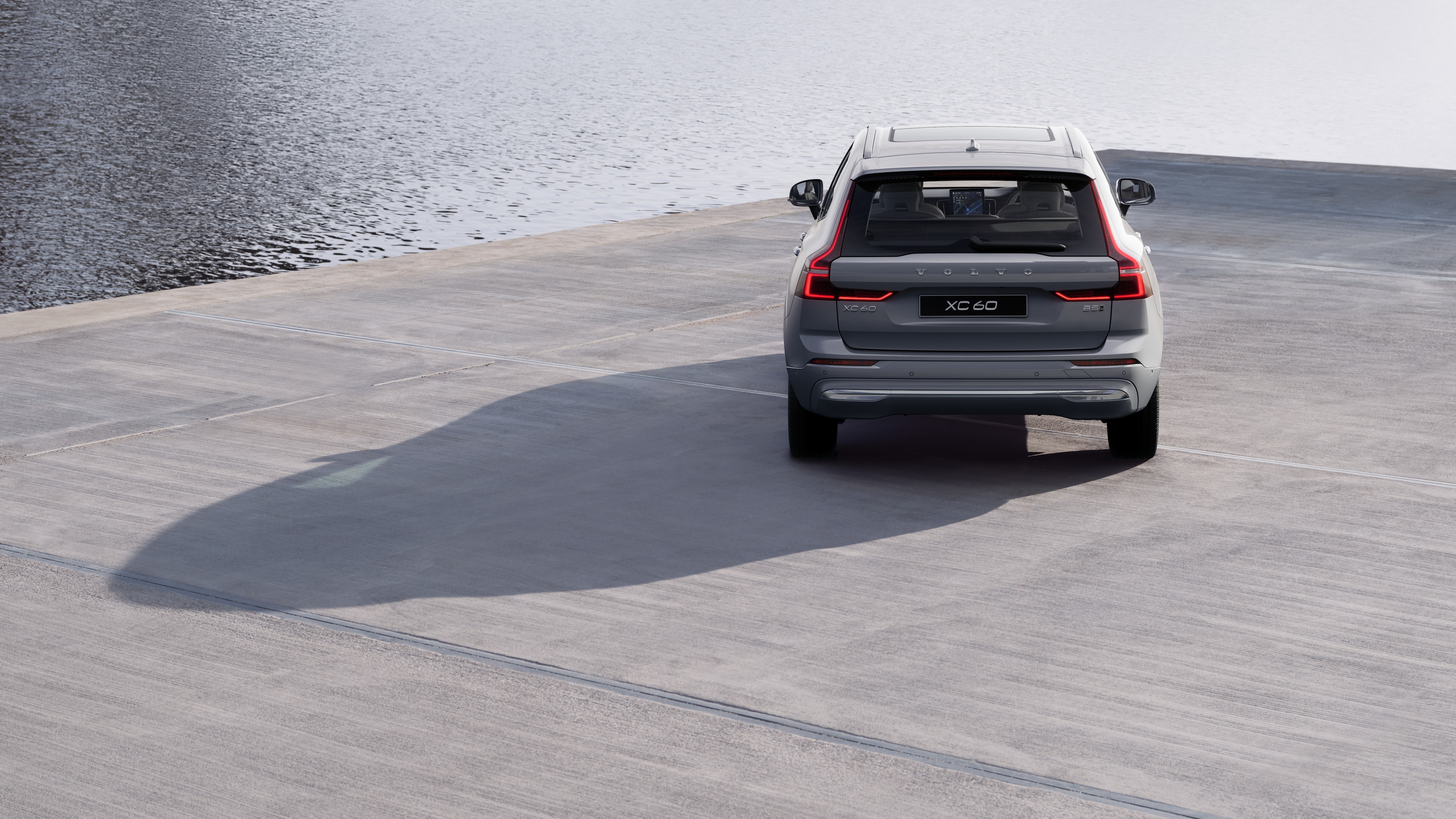 Volvo car rear view on a winding coastal road with a beachside background.