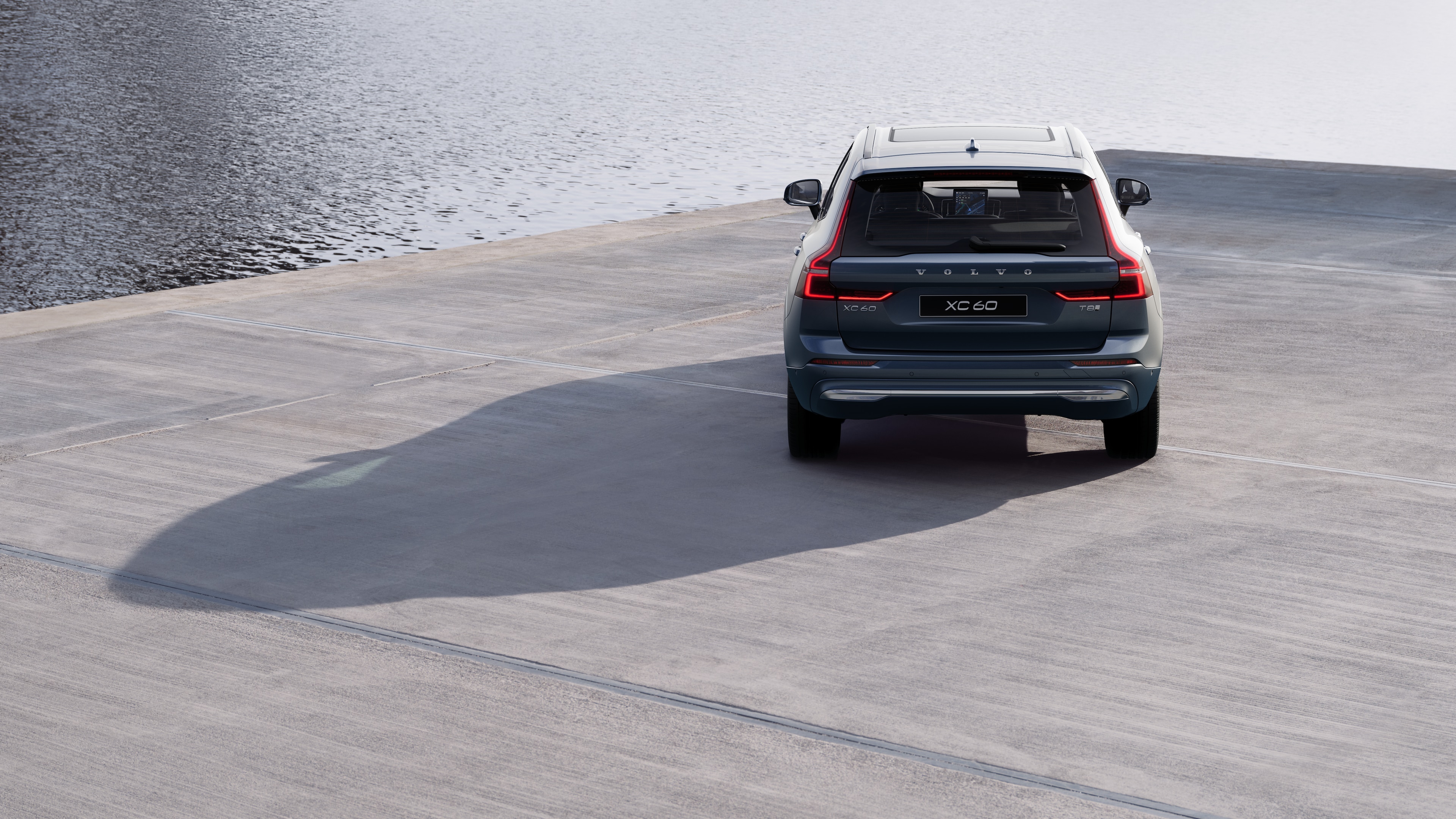 Horft aftan á Volvo-bíl á bugðóttum strandvegi með bakgrunn við ströndina.