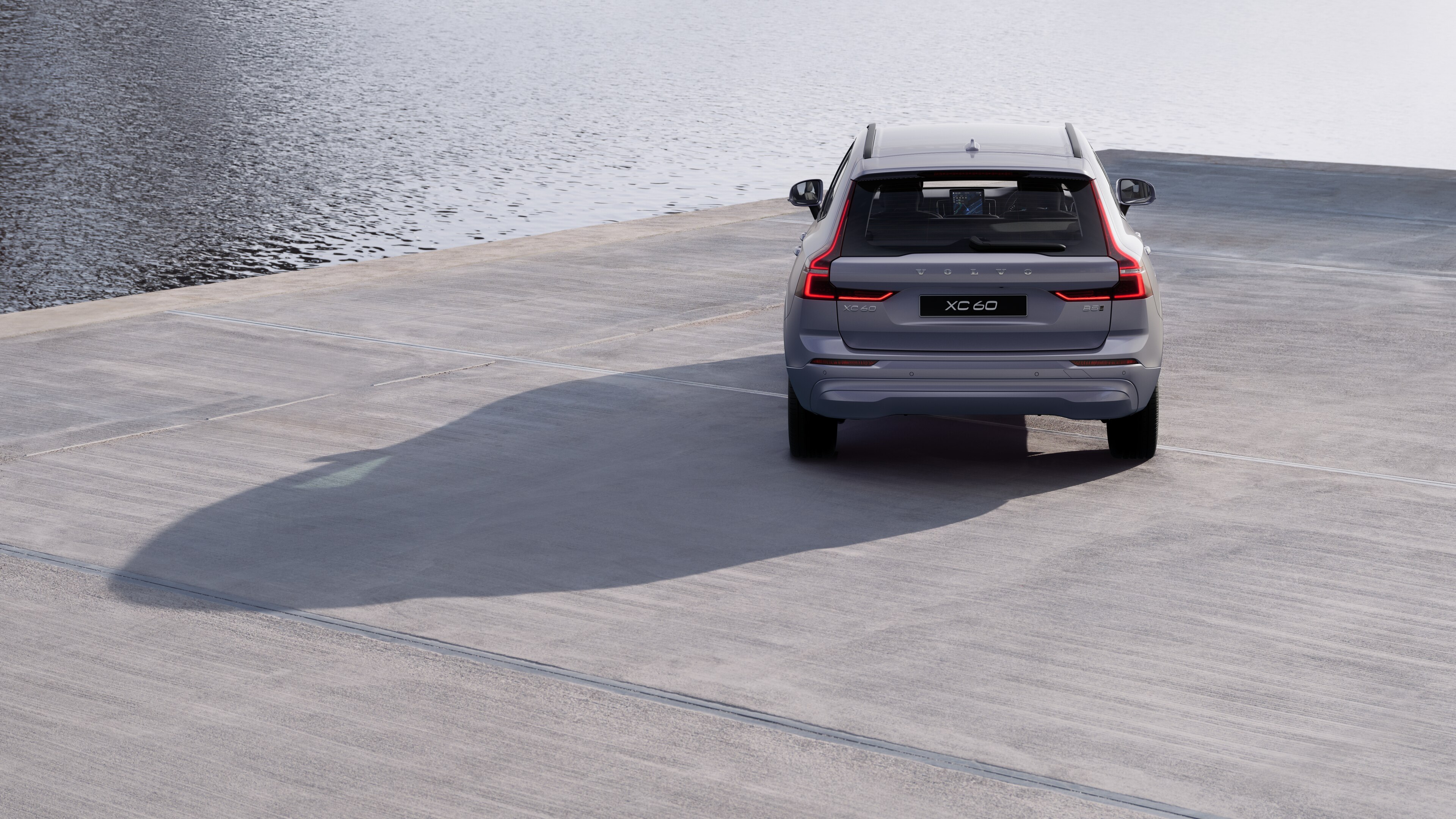 Volvo car rear view on a winding coastal road with a beachside background.