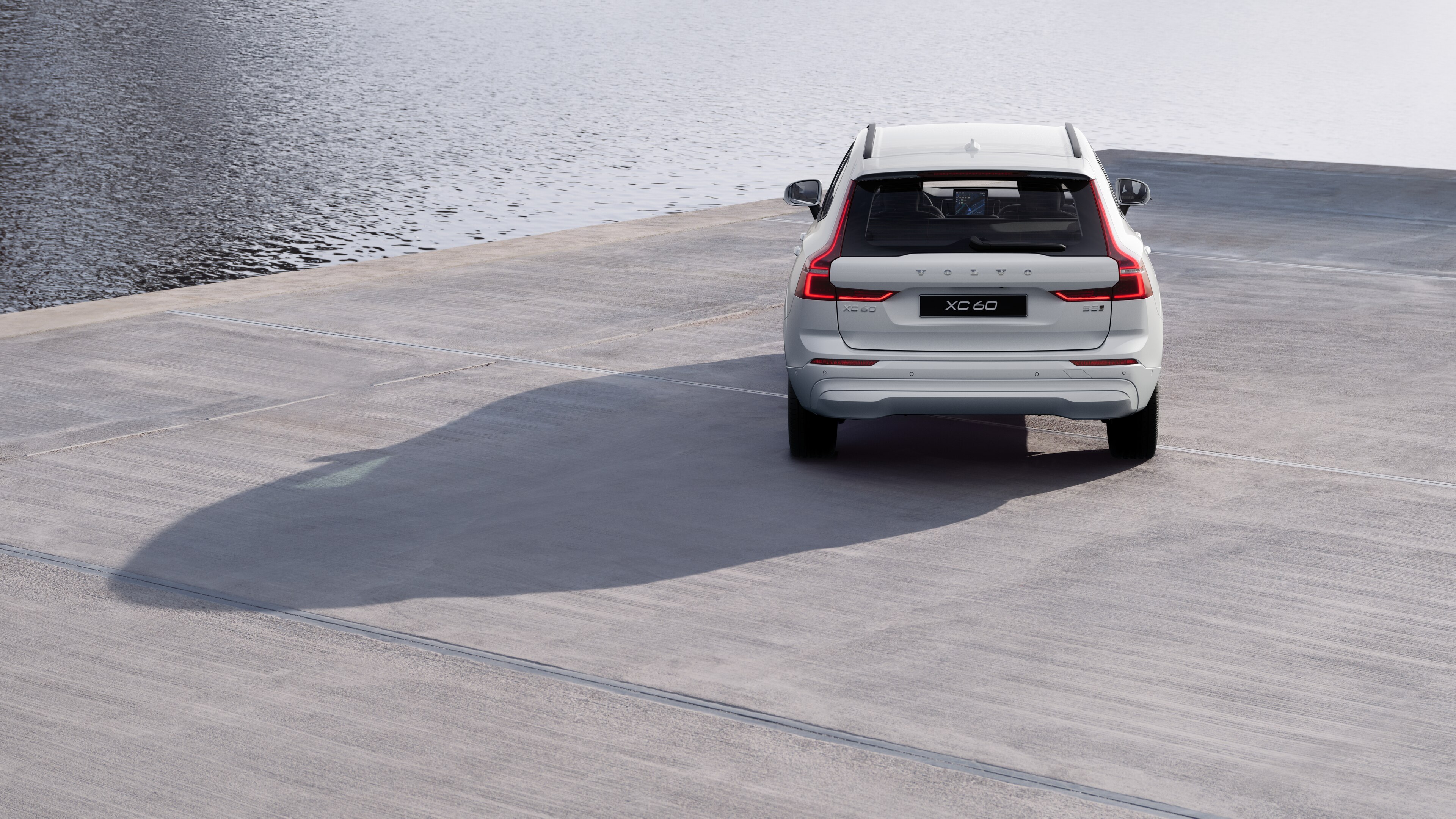 Volvo car rear view on a winding coastal road with a beachside background.