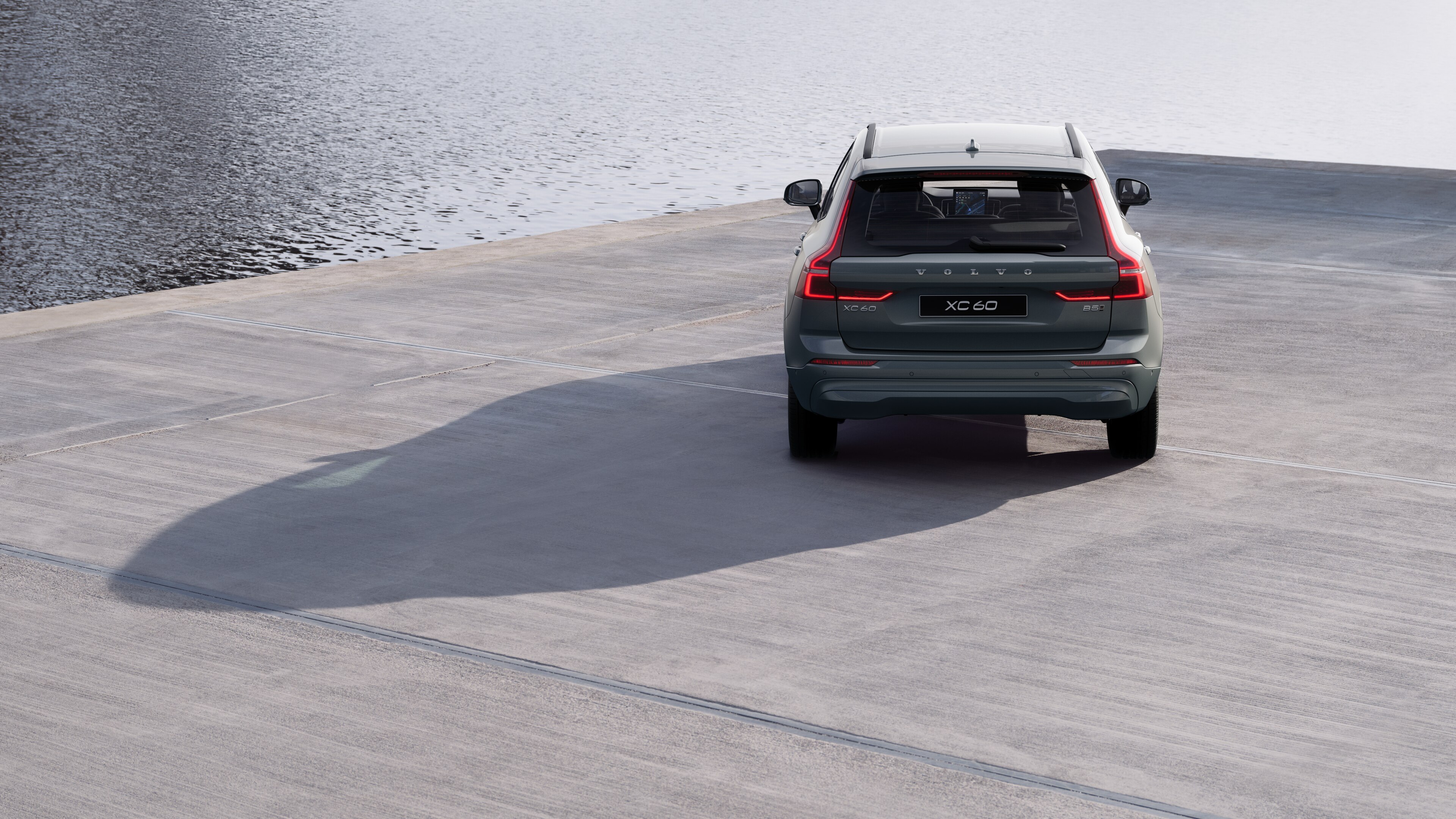 Volvo car rear view on a winding coastal road with a beachside background.