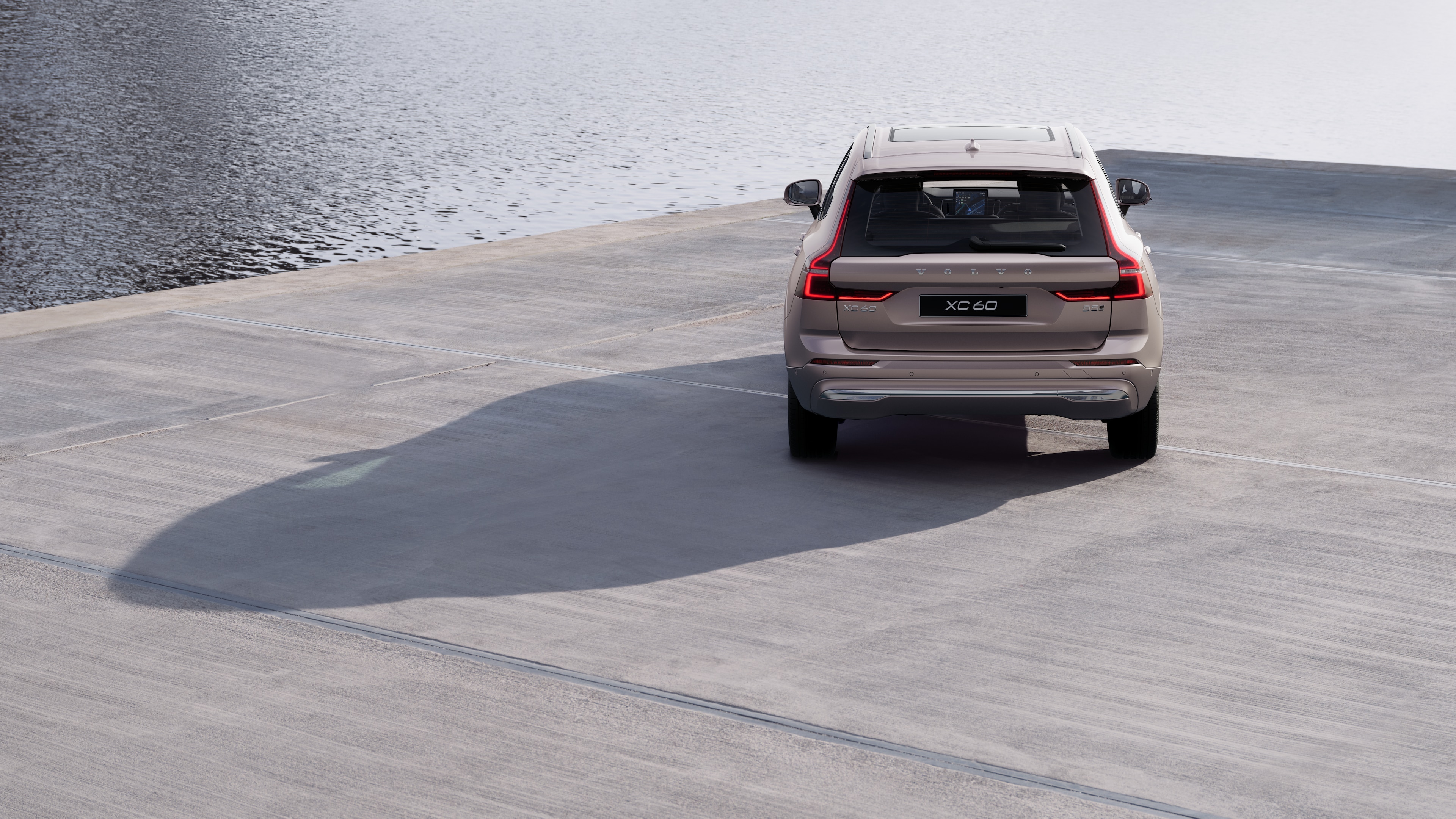 Hình ảnh phía sau xe Volvo trên con đường ven biển quanh co với phông nền bên bờ biển.