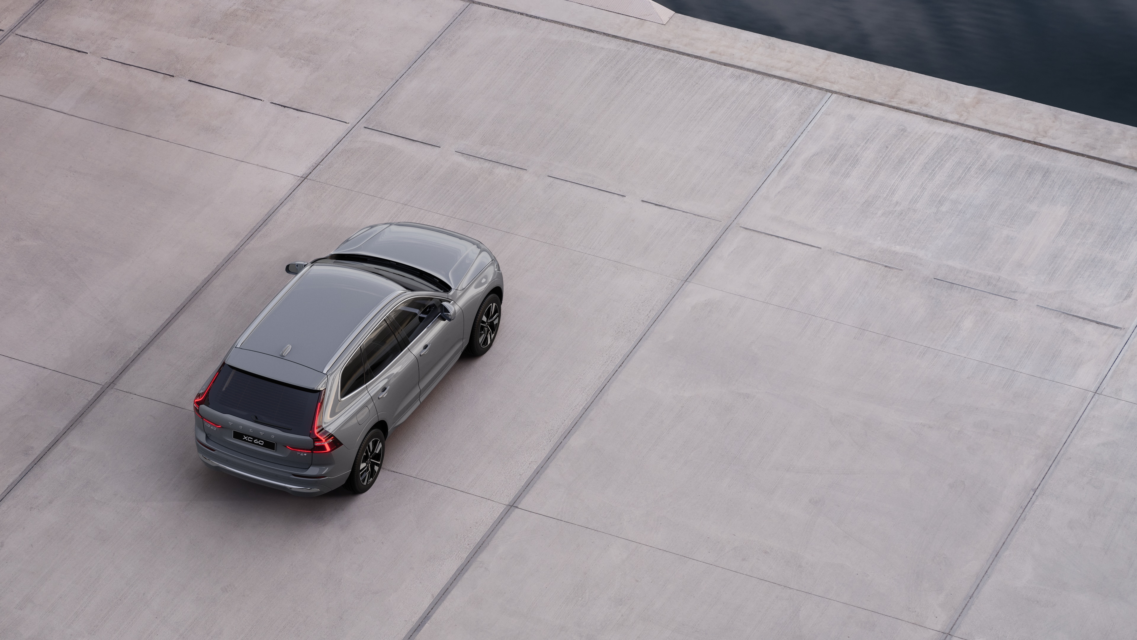 Volvo-bil sett bakfra parkert i en rolig gate ved vannet med asfaltert gangvei og vann som bakgrunn.