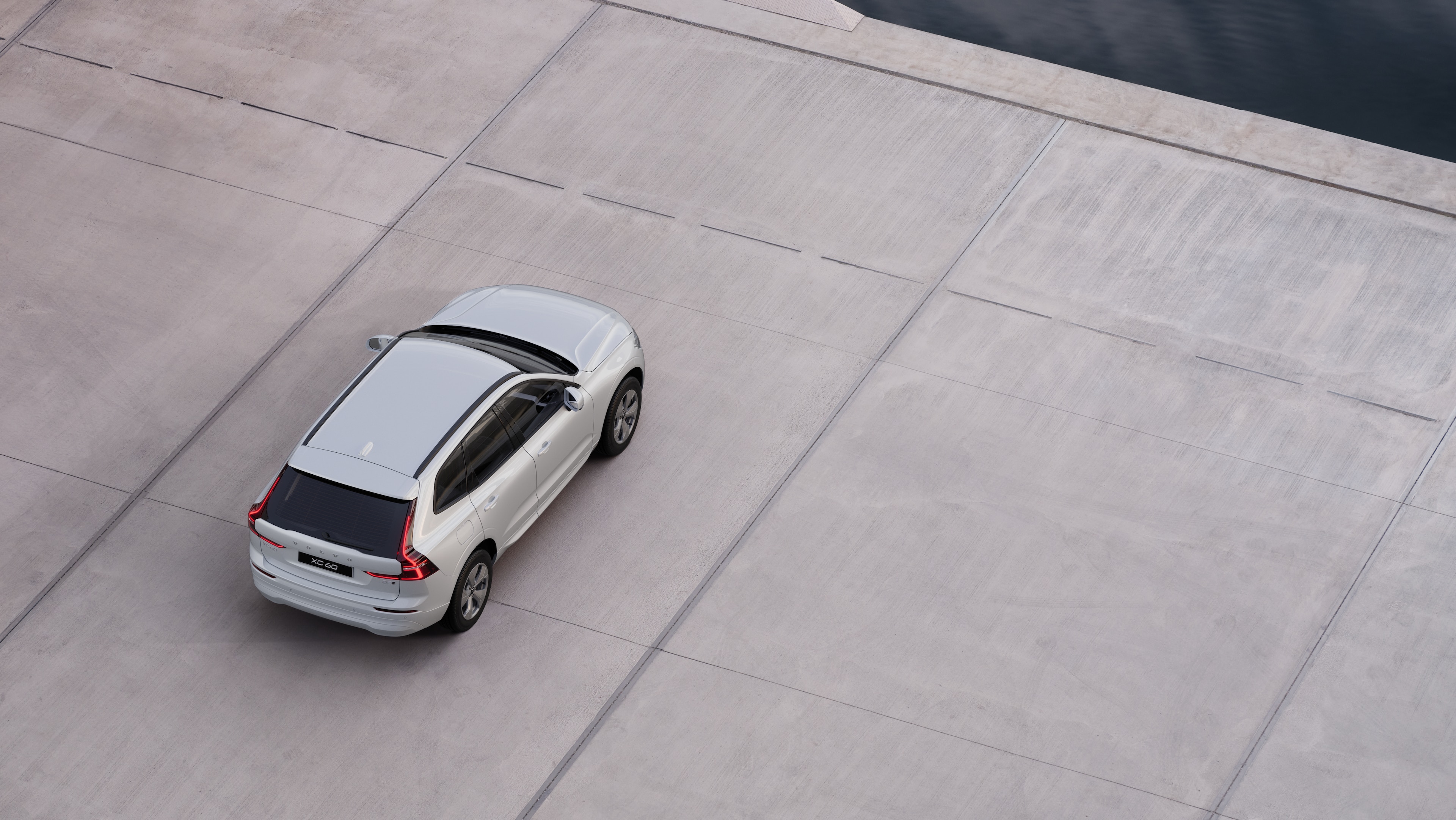 Vista posteriore di una Volvo parcheggiata in una strada tranquilla accanto all'acqua, con un passaggio pedonale lastricato e l'acqua sullo sfondo.