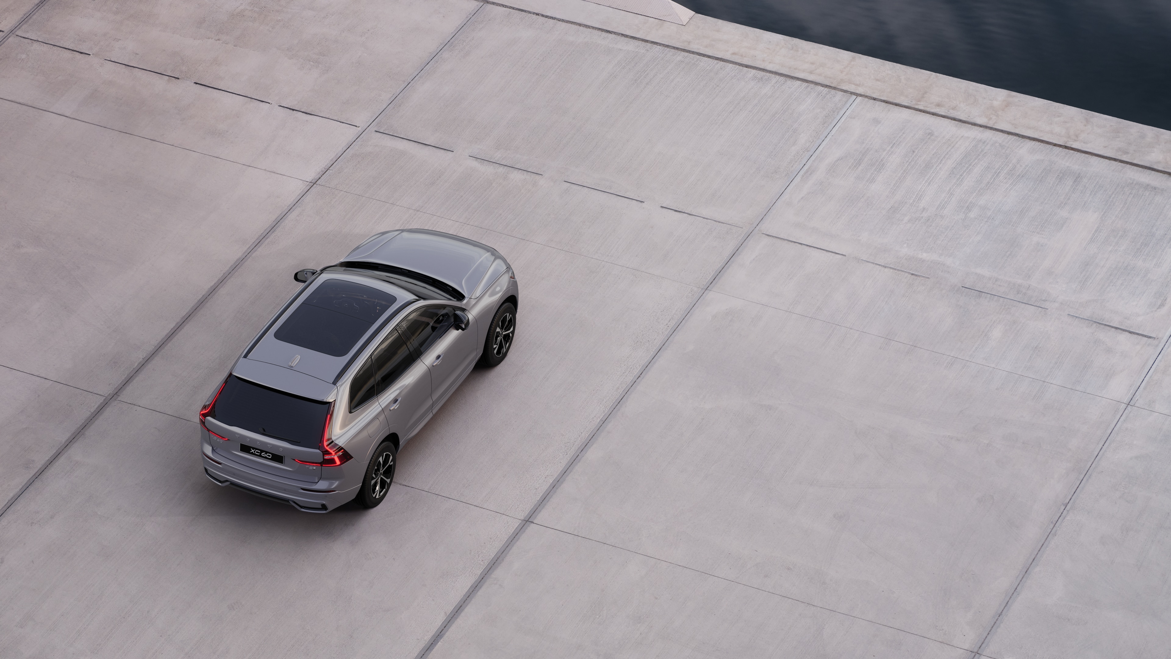 Volvo car rear view parked on quiet street beside water, with a paved walkway and water as the background.