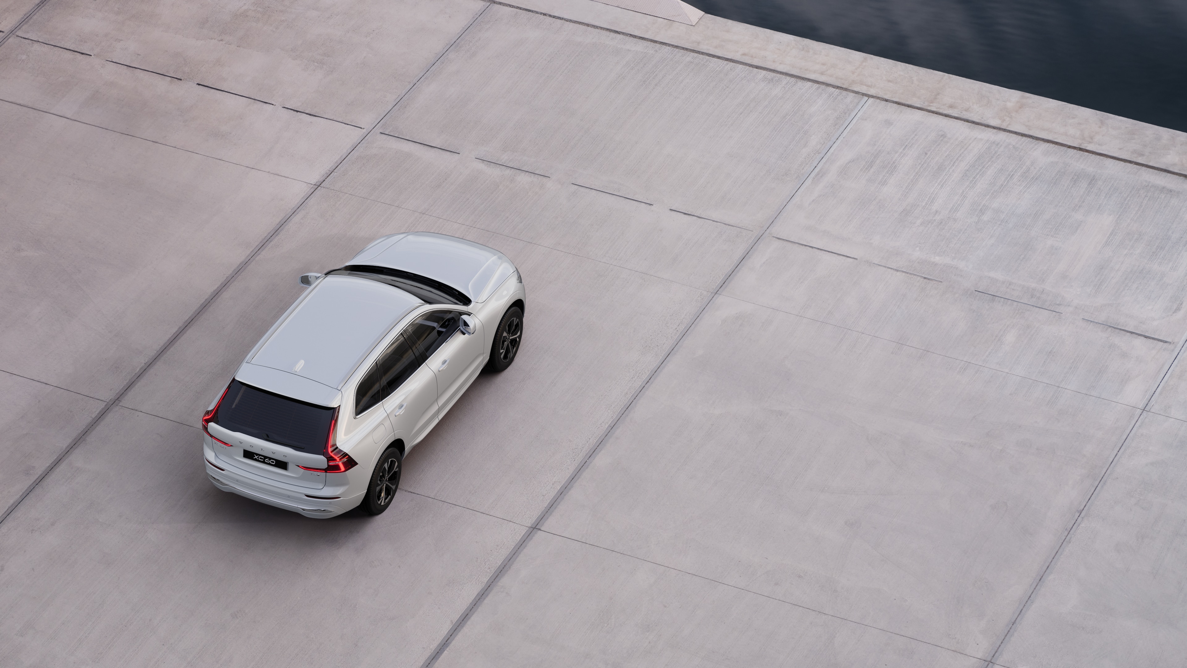 Vue arrière d’une Volvo garée dans une rue calme au bord de l’eau, avec une allée pavée et de l’eau en arrière-plan.