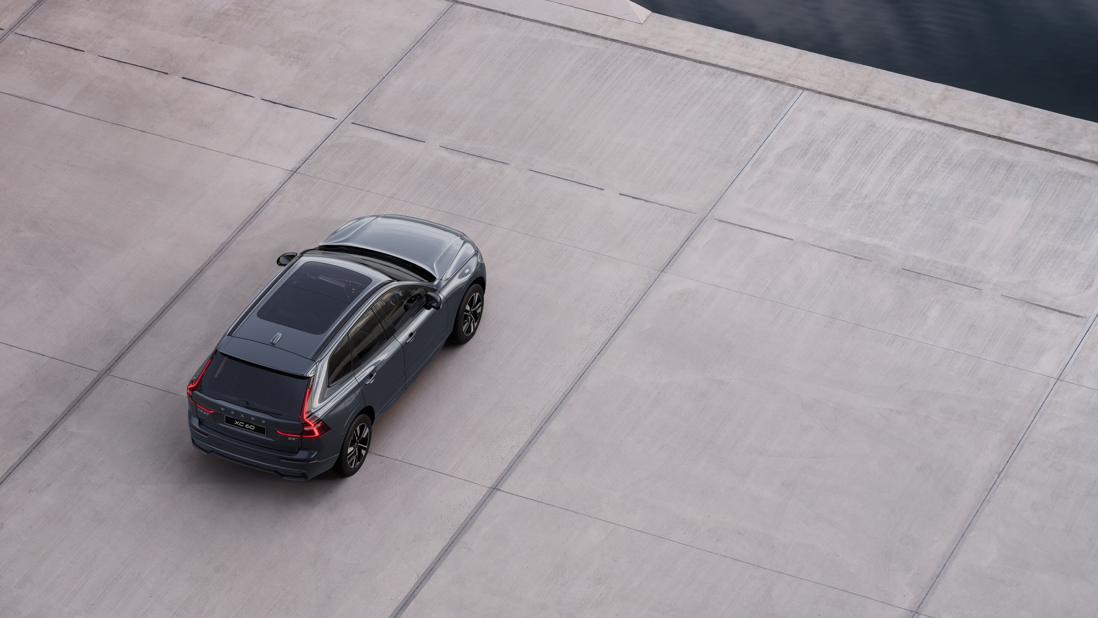 Volvo car rear view parked on quiet street beside water, with a paved walkway and water as the background.