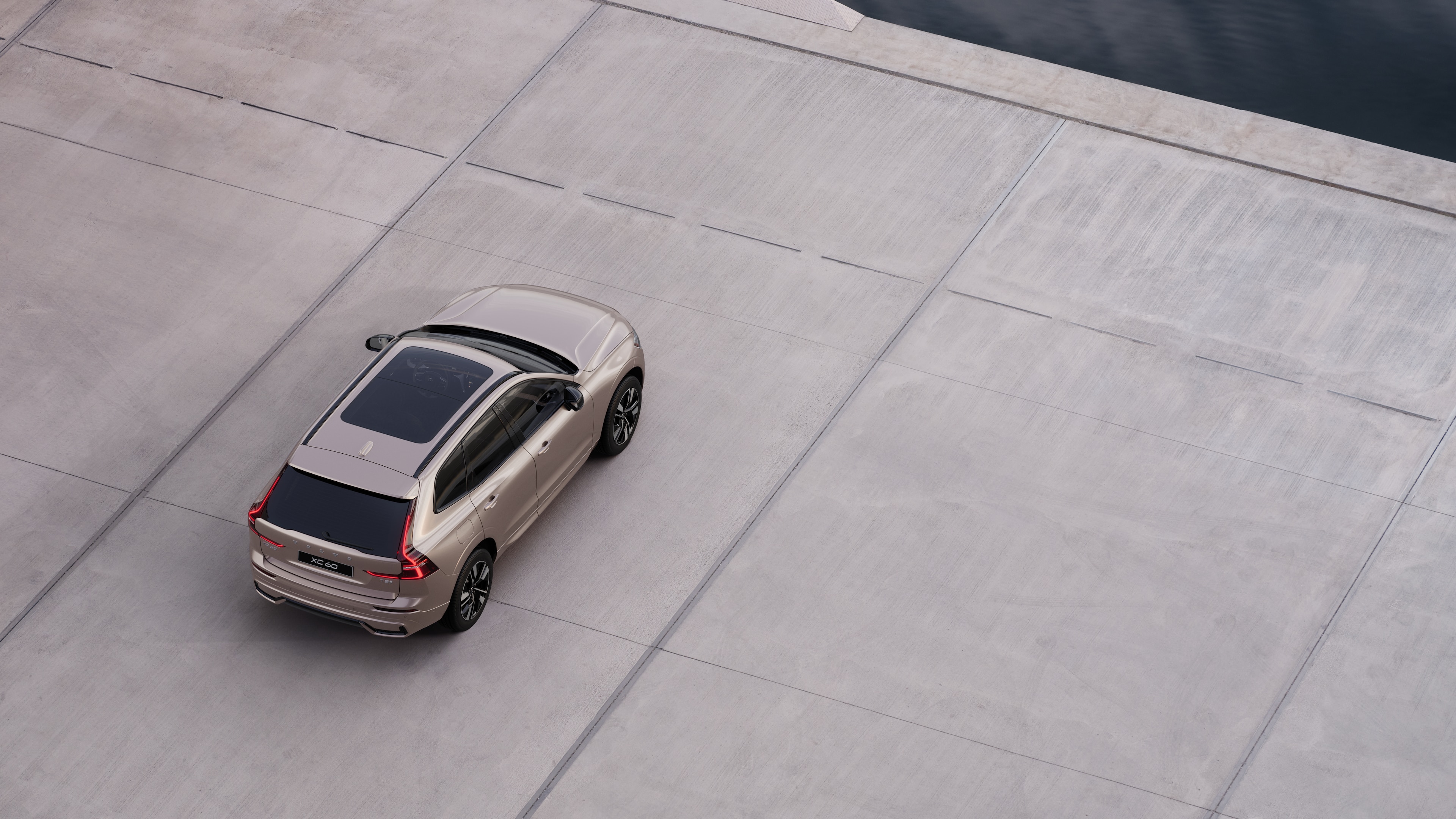 Volvo car rear view parked on quiet street beside water, with a paved walkway and water as the background.