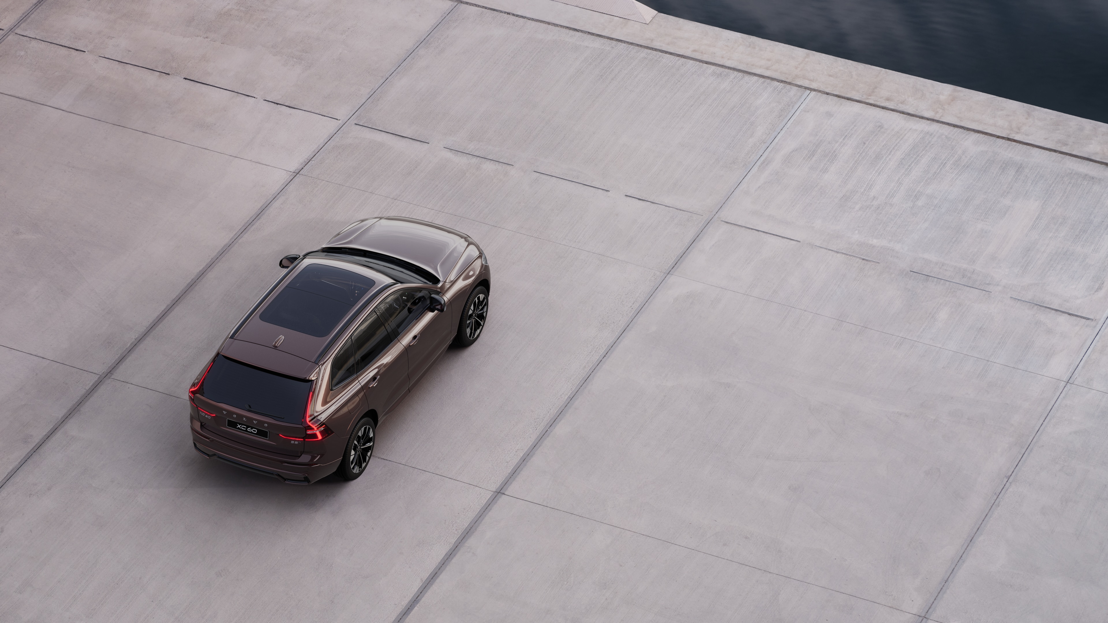 Volvo car rear view parked on quiet street beside water, with a paved walkway and water as the background.