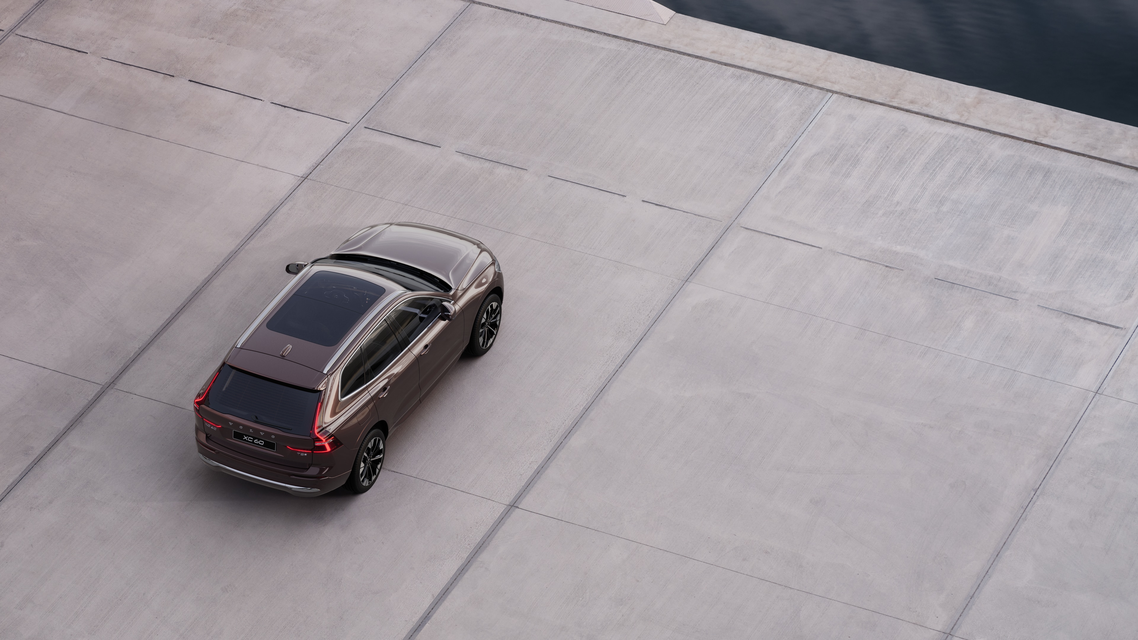 Автомобіль Volvo, вигляд ззаду, припаркований на тихій вулиці біля води, на тлі асфальтованої доріжки та води.