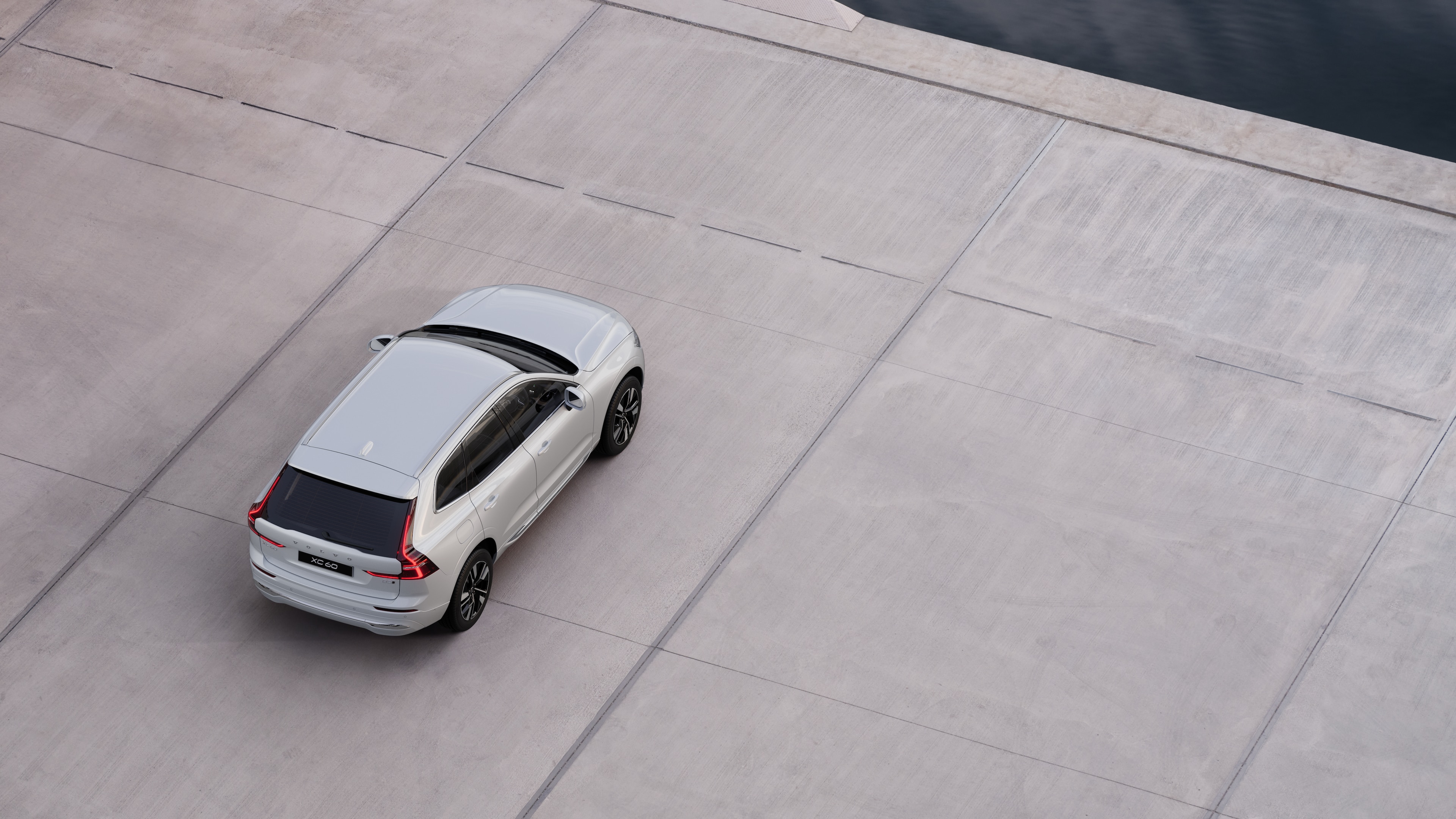 Volvo car rear view parked on quiet street beside water, with a paved walkway and water as the background.