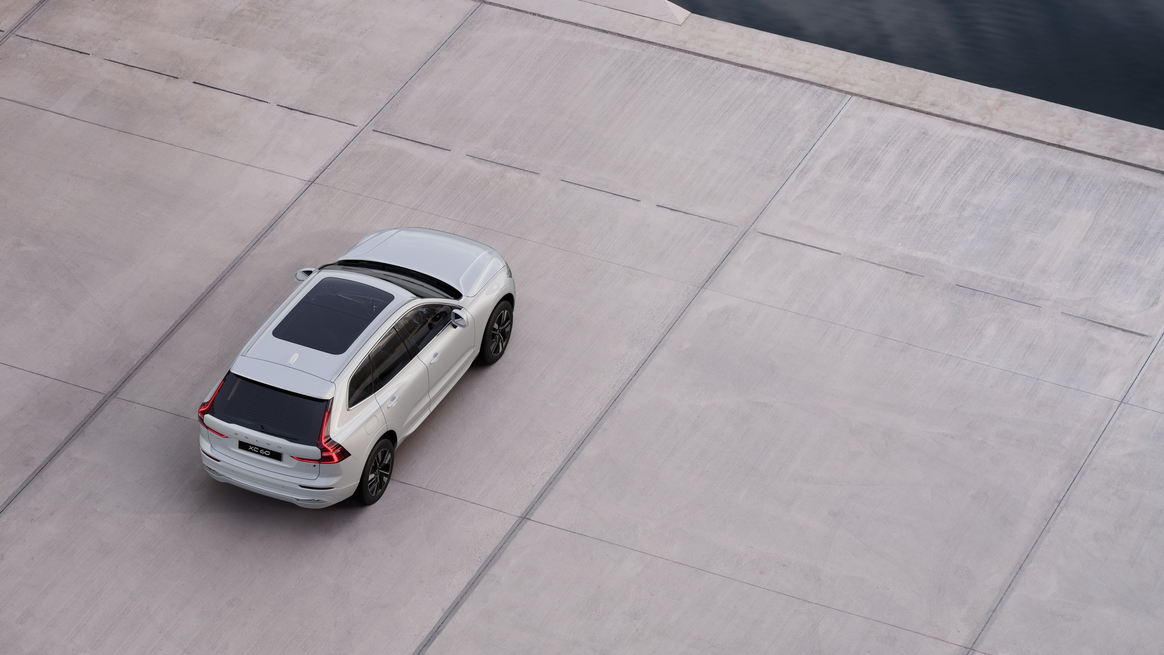Volvo car rear view parked on quiet street beside water, with a paved walkway and water as the background.