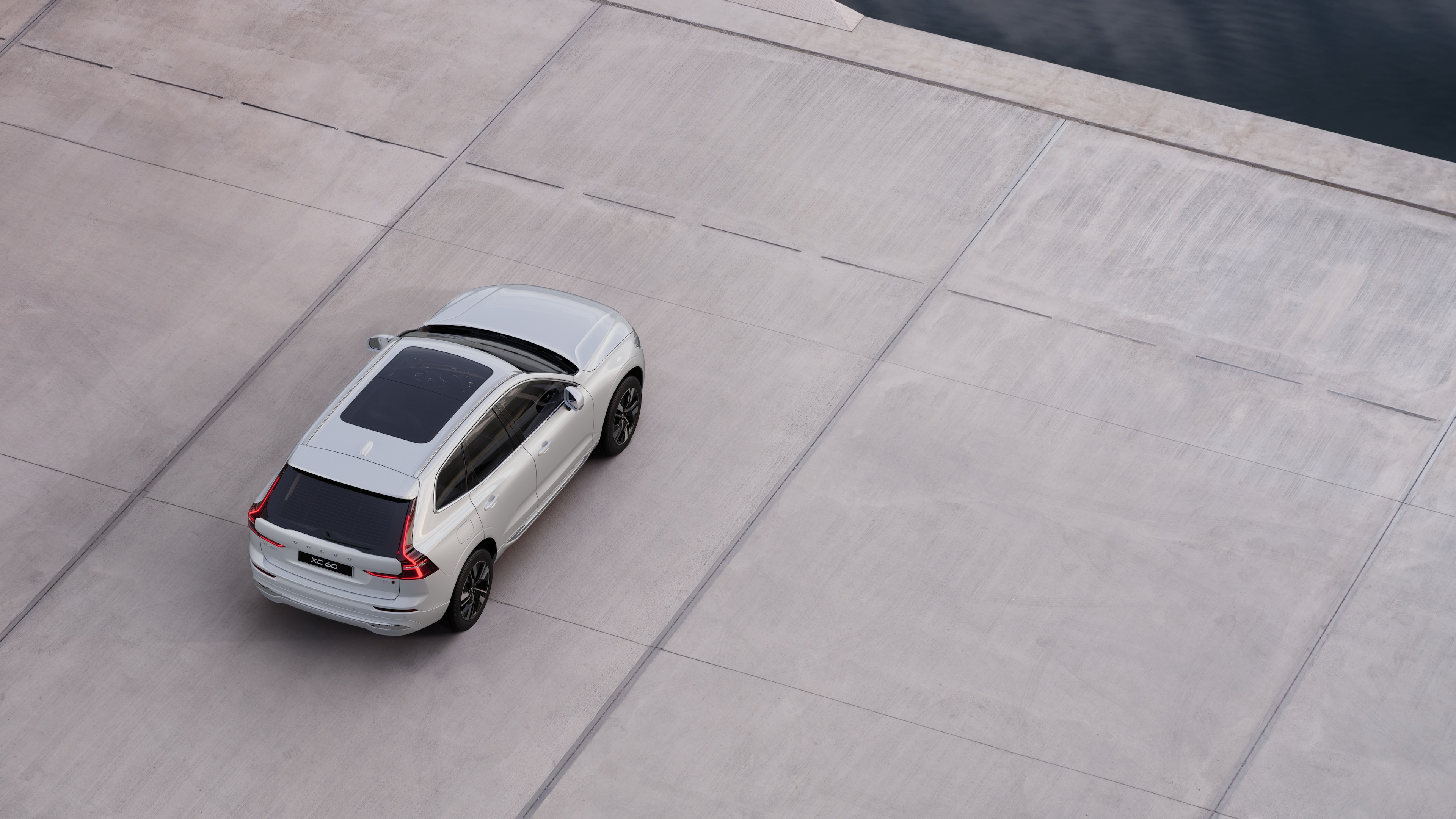 Mặt sau xe Volvo đỗ trên con phố yên tĩnh bên cạnh mặt nước, với lối đi lát đá và nước làm nền.